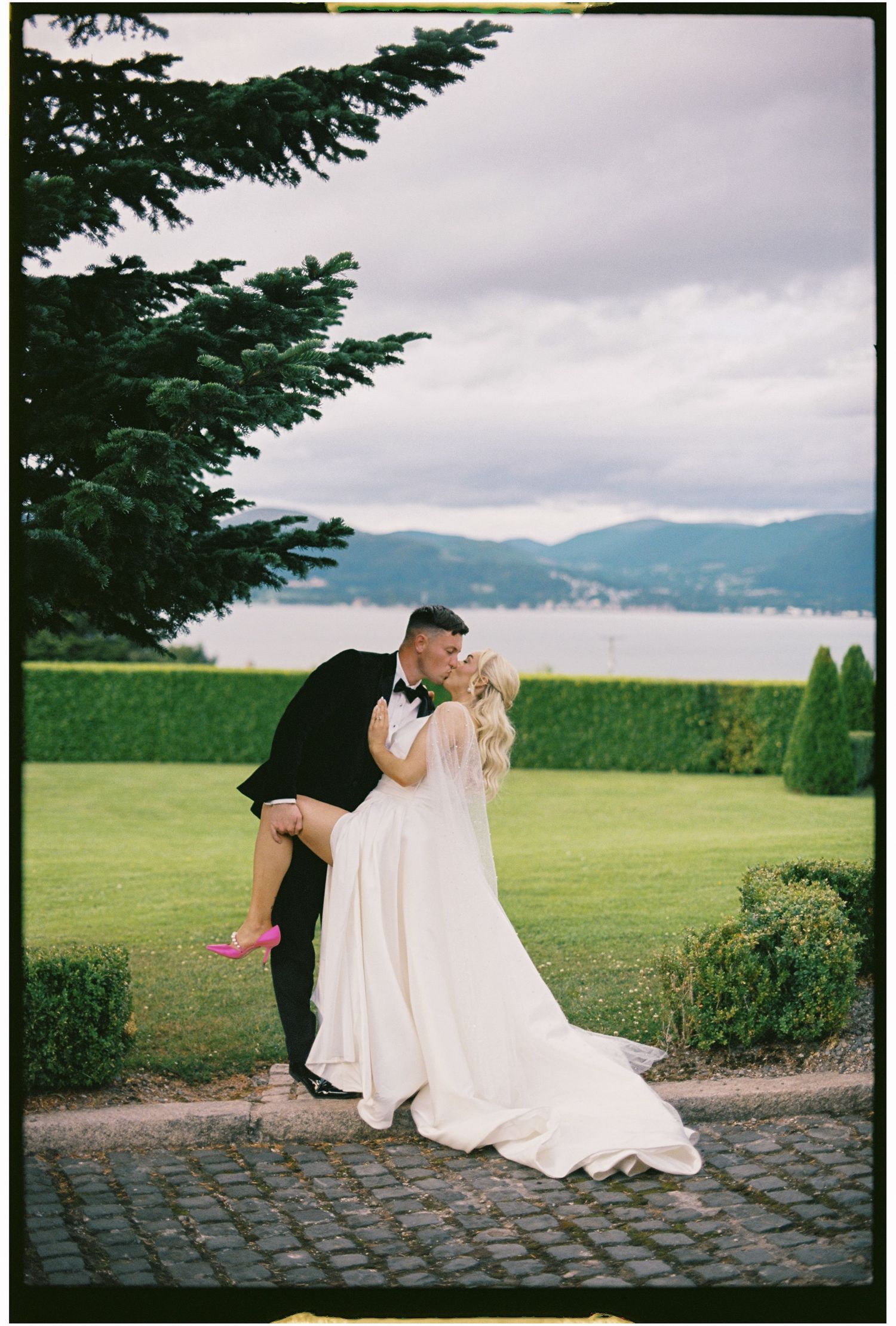 A couple shares an intimate moment on a stone path overlooking mountains and a lake on their wedding day.