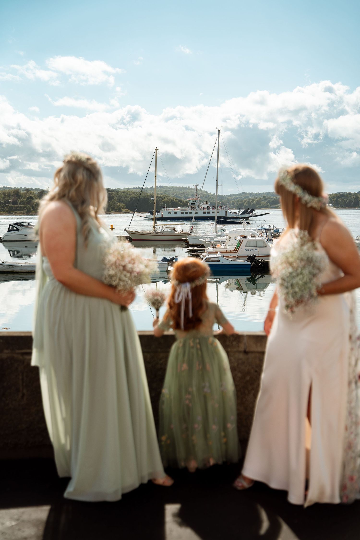 Bridesmaids in light dresses overlooking a marina with boats in the background.
