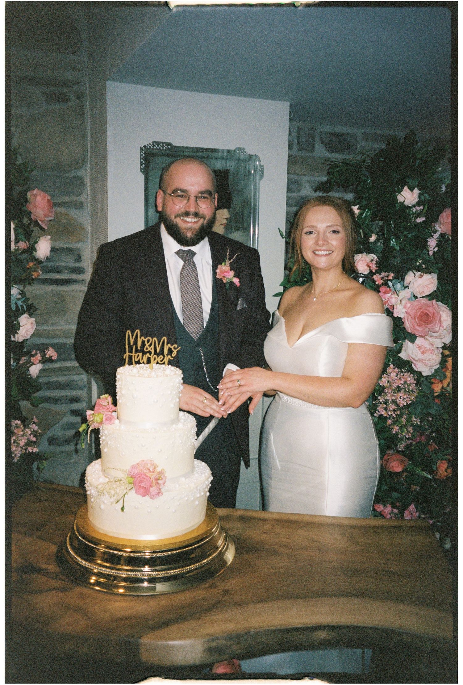 Wedding couple cutting their elegant white and pink floral wedding cake at a rustic indoor reception venue.