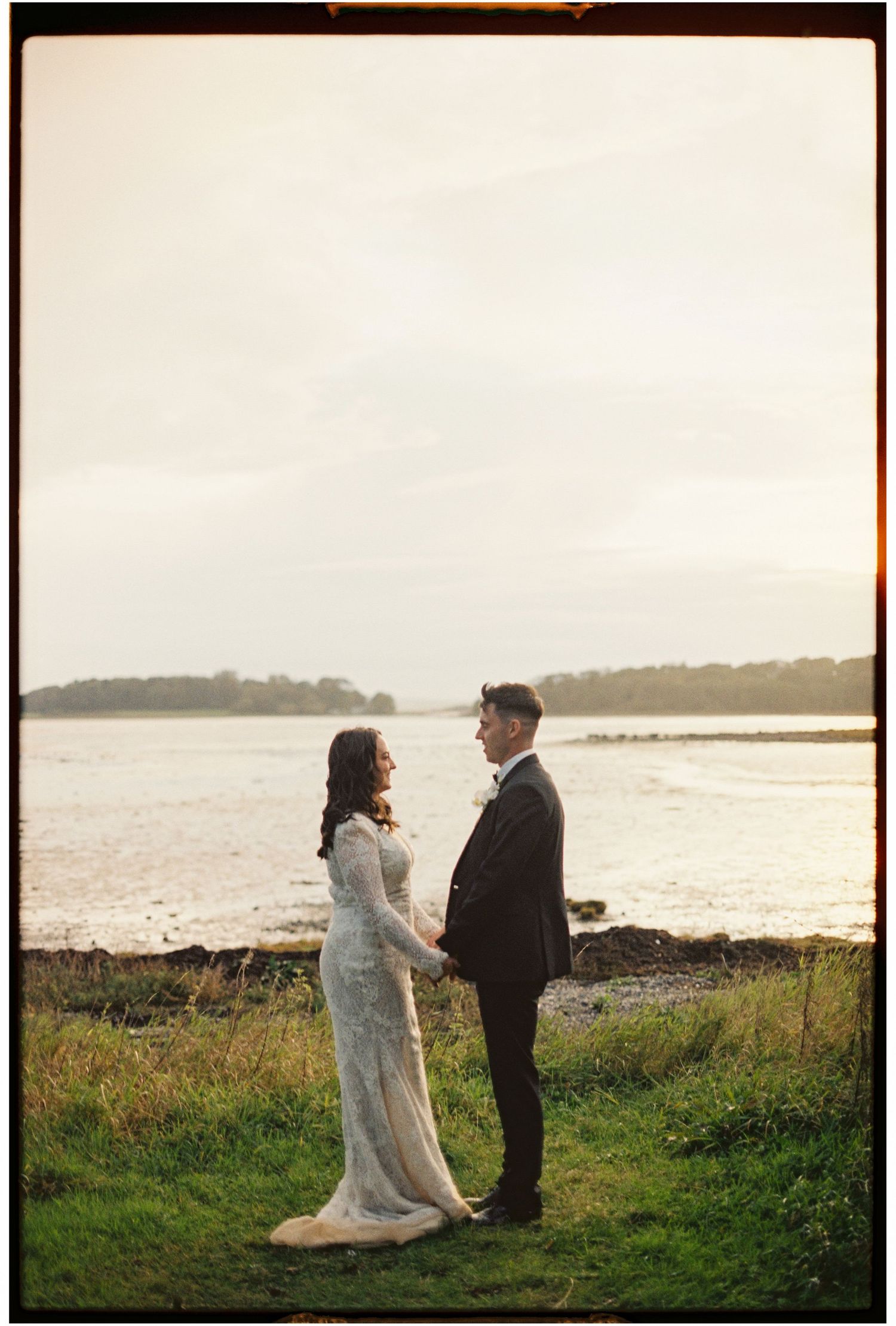 Couple shares intimate moment on coastal cliff during sunset wedding photoshoot.