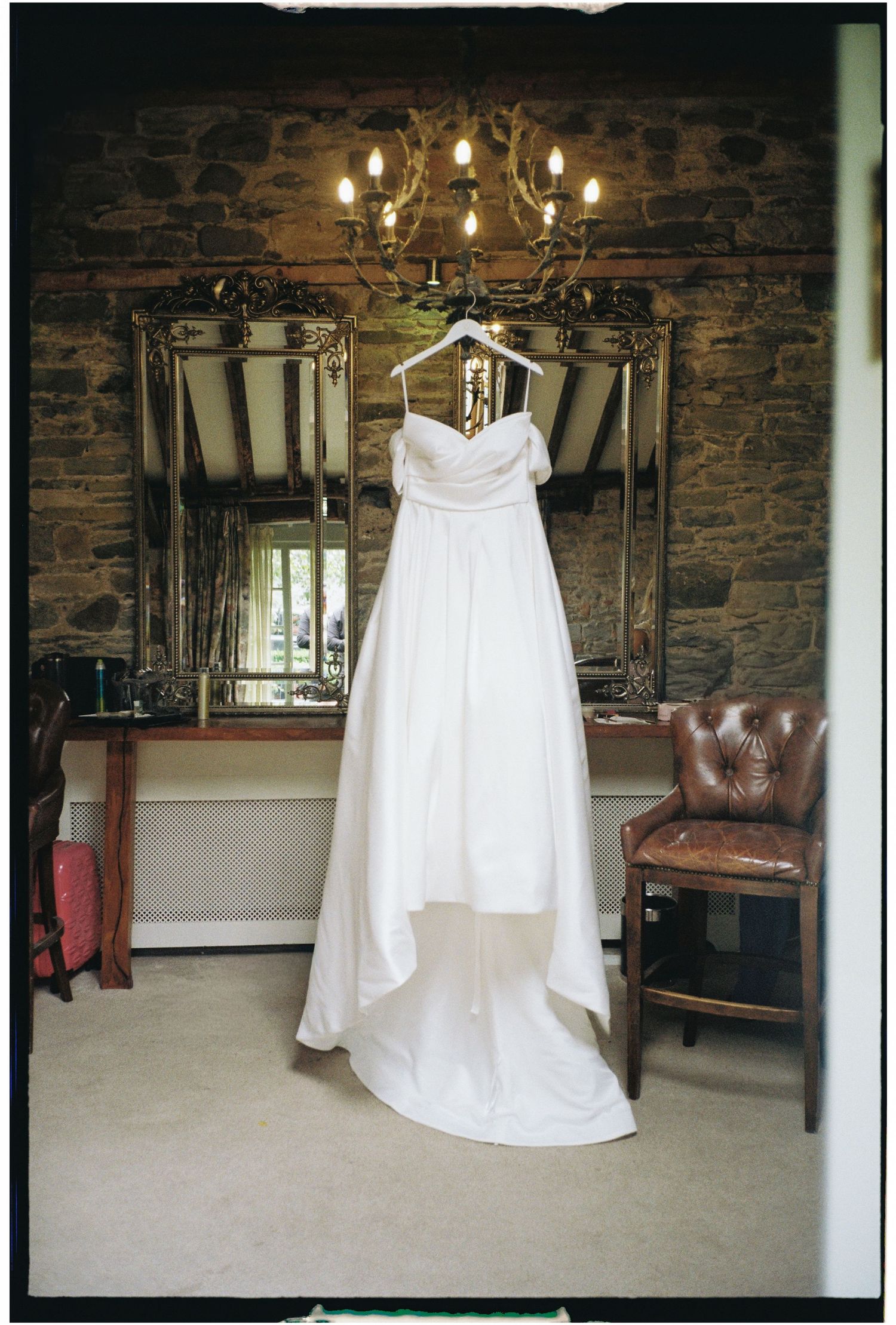 A white wedding dress hangs elegantly in a rustic room with exposed brick walls and leather furniture.