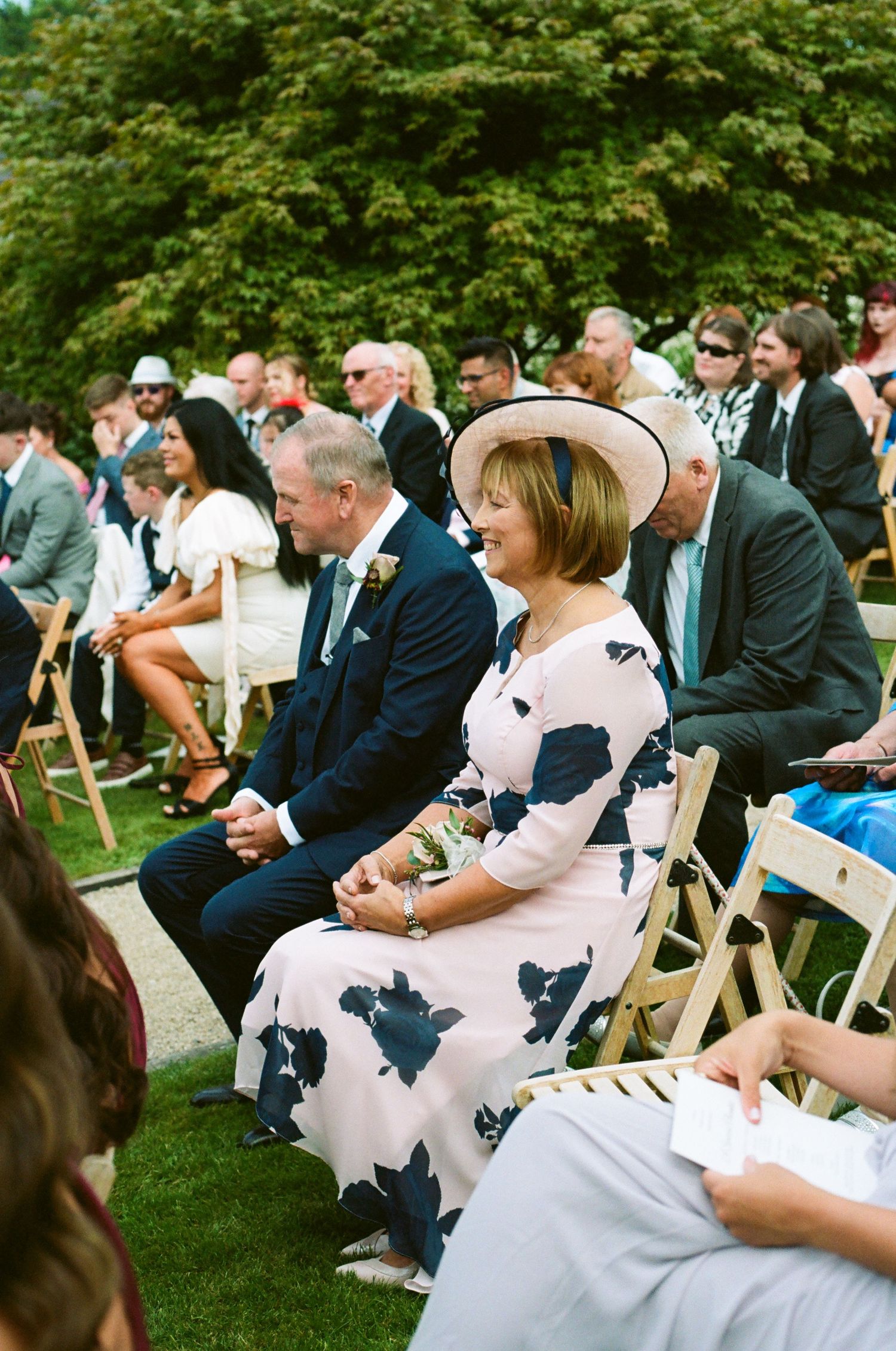 Wedding guests seated on white folding chairs during an outdoor garden ceremony.