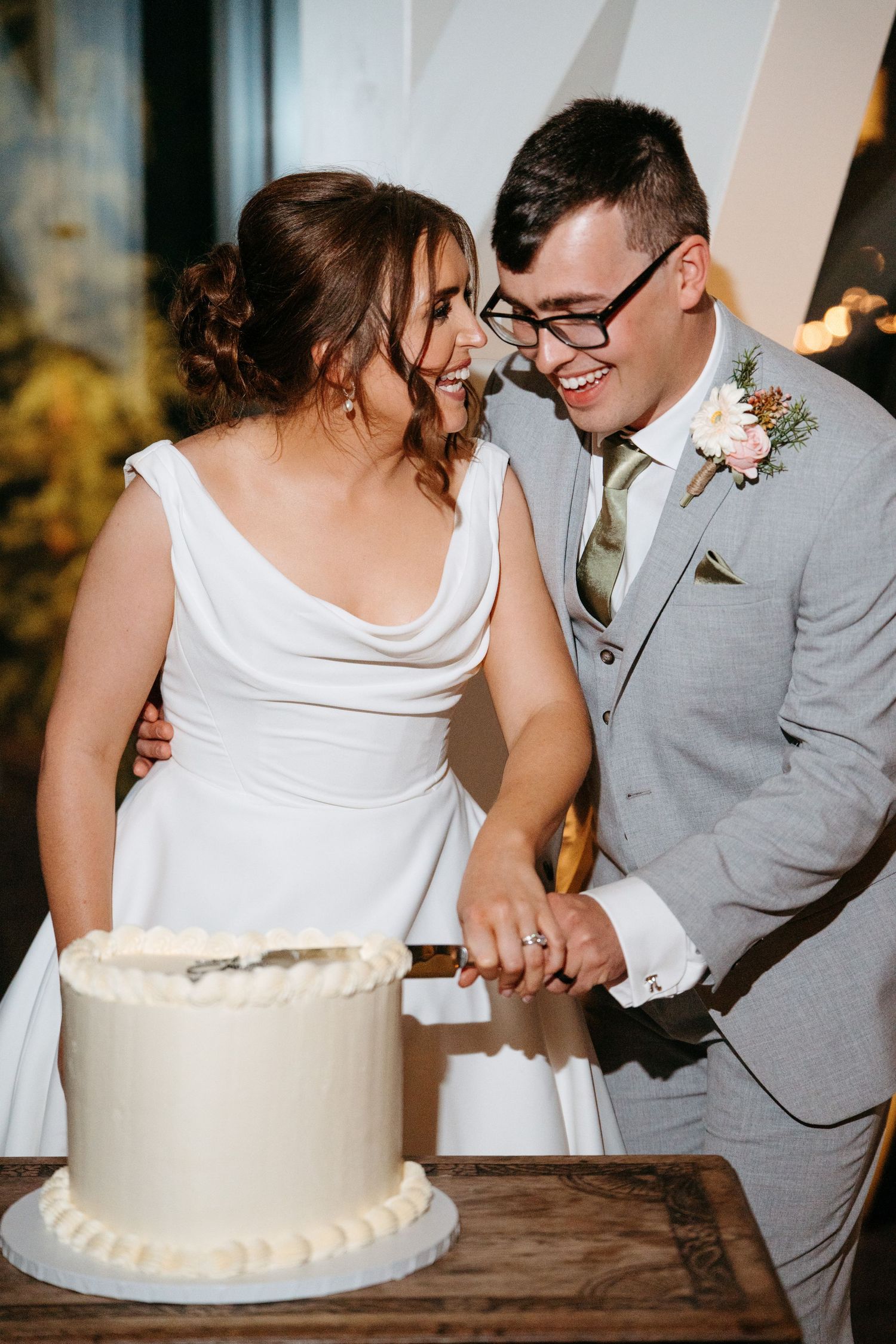 Newlyweds share an intimate moment while cutting their white wedding cake at a rustic reception.