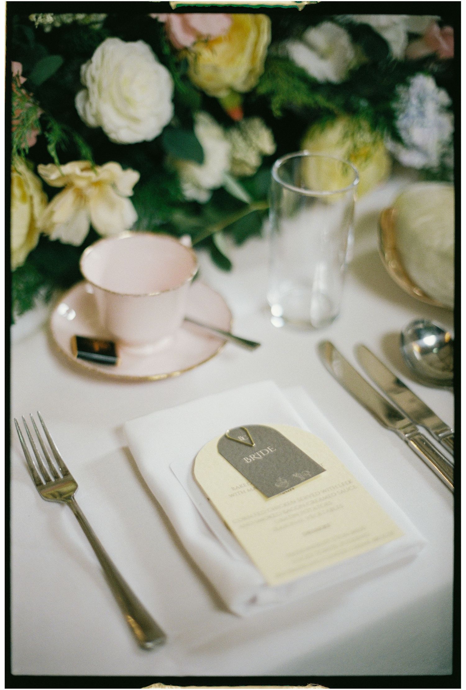 Elegant wedding place setting with white flowers, silverware and name cards on crisp white linens.