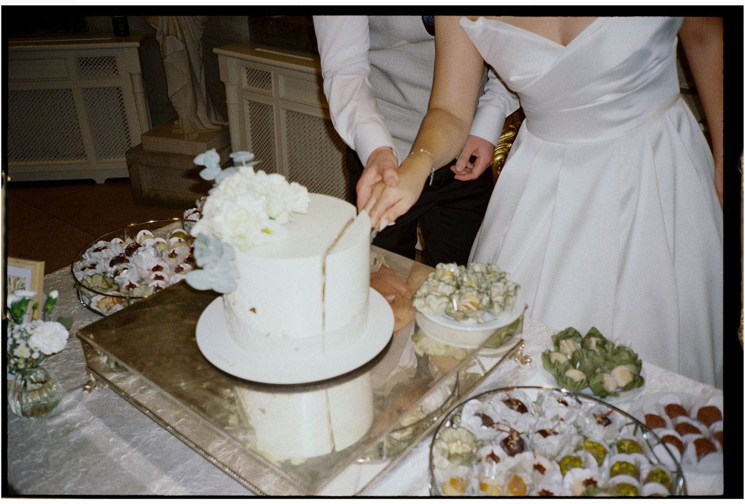 A couple cuts into their elegant white wedding cake at the reception.