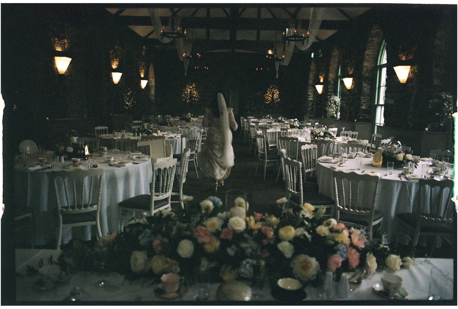Elegant wedding reception venue with round tables and floral arrangements in a dimly lit room.