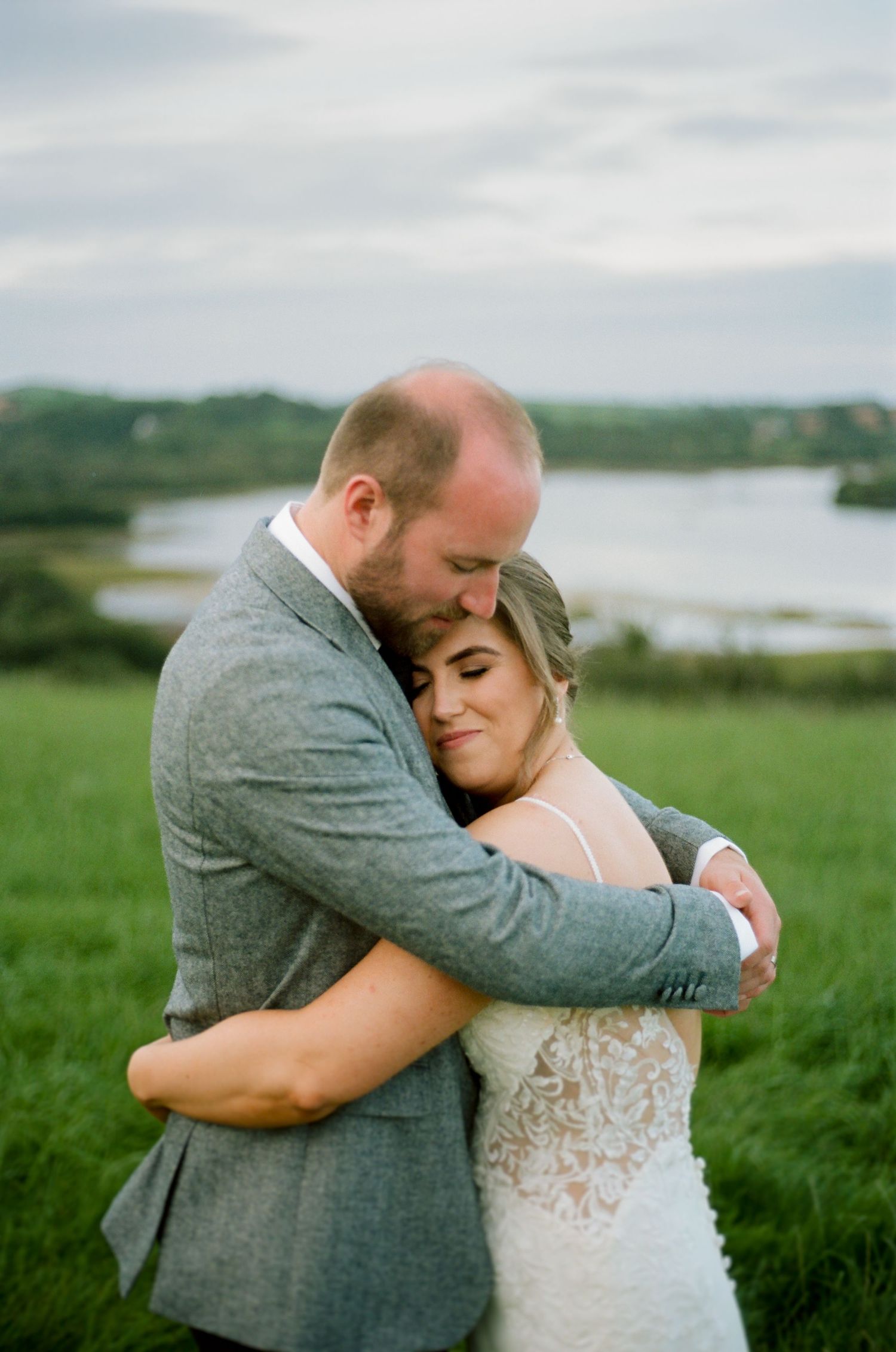 A tender embrace between newlyweds against a scenic coastal landscape with rolling green hills.