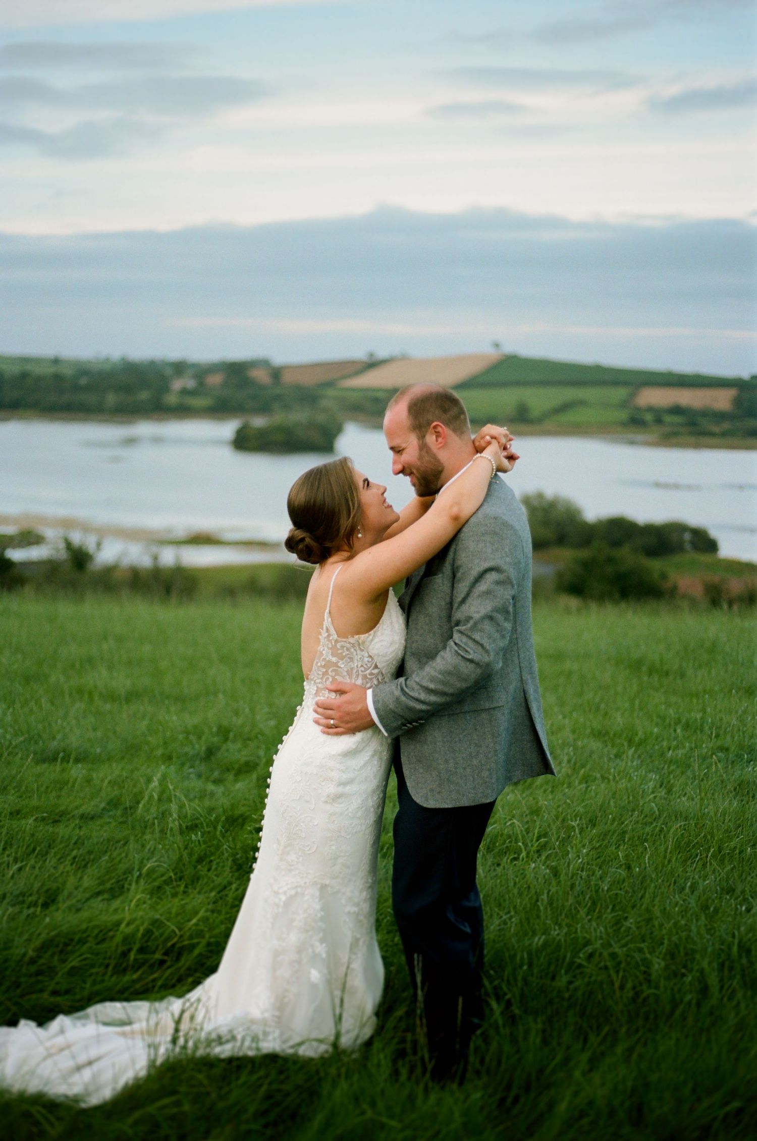 A couple embraces on a hilltop overlooking a scenic lake and rolling countryside.