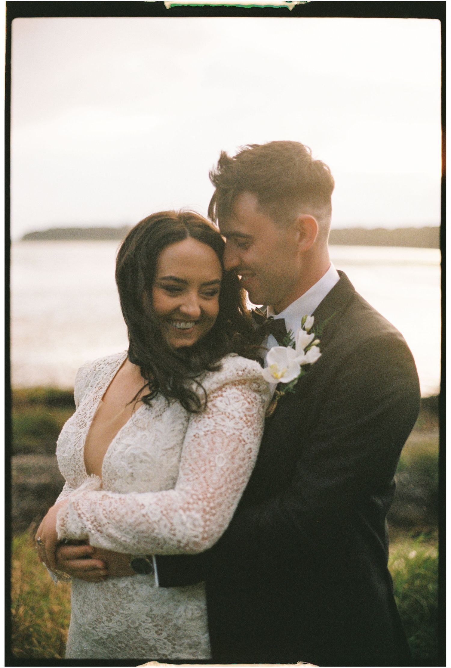 Romantic sunset moment captured between newlyweds in formal wedding attire by the coast.