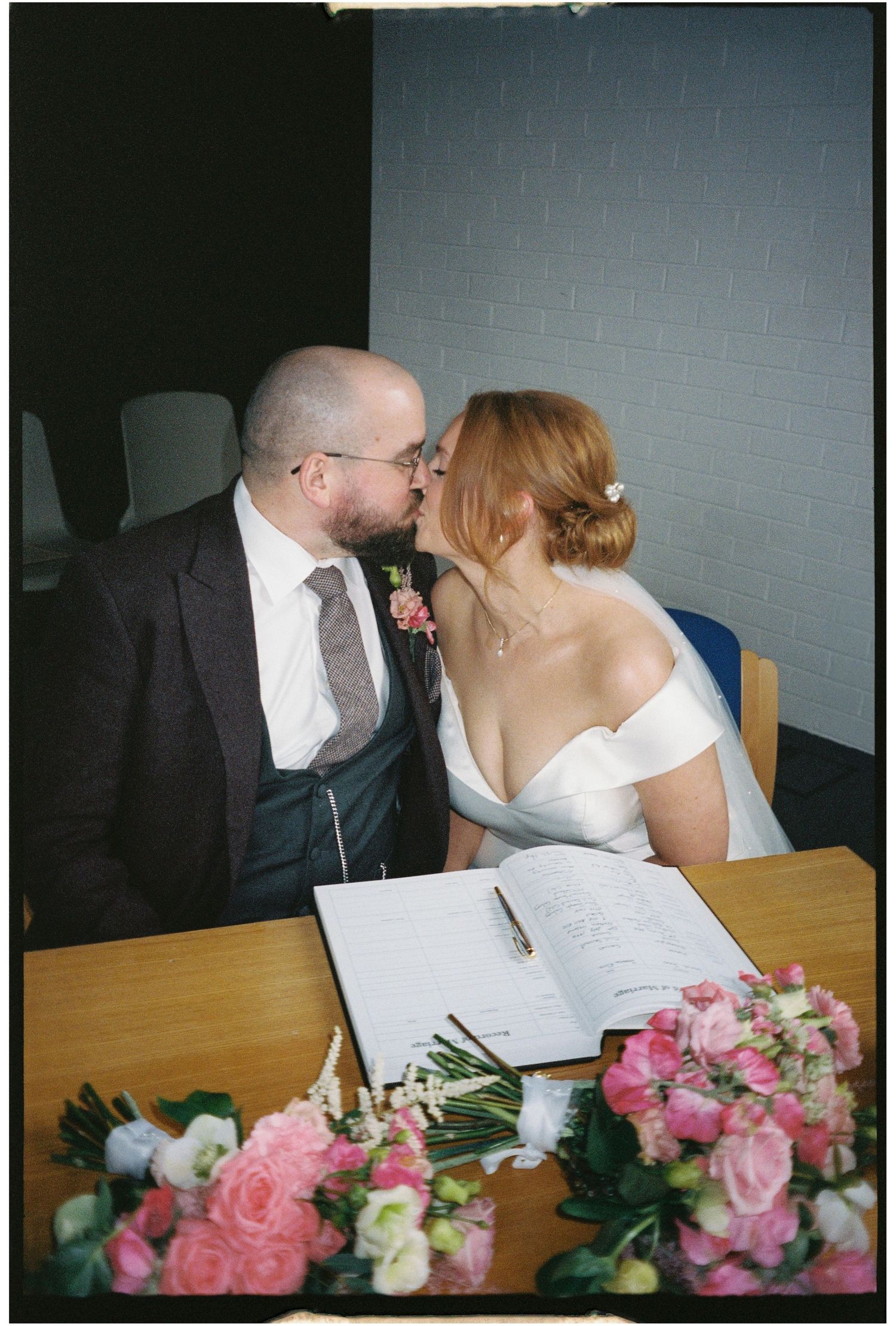 Wedding couple signing documents at a table decorated with pink roses and white flowers.