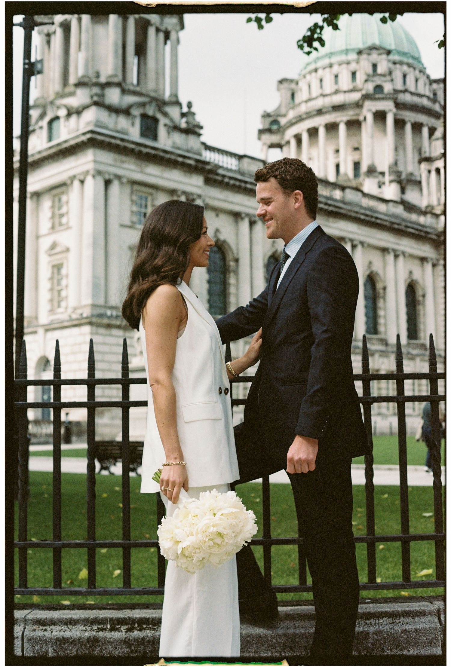 A romantic wedding couple shares tender moments in front of Belfast City Hall's elegant architecture.