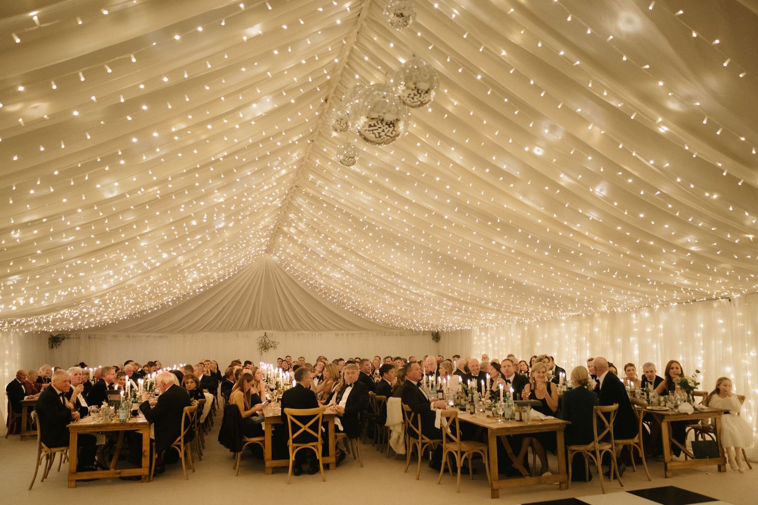 Elegant wedding reception venue with white fabric draping and twinkling string lights creating a romantic ceiling canopy.