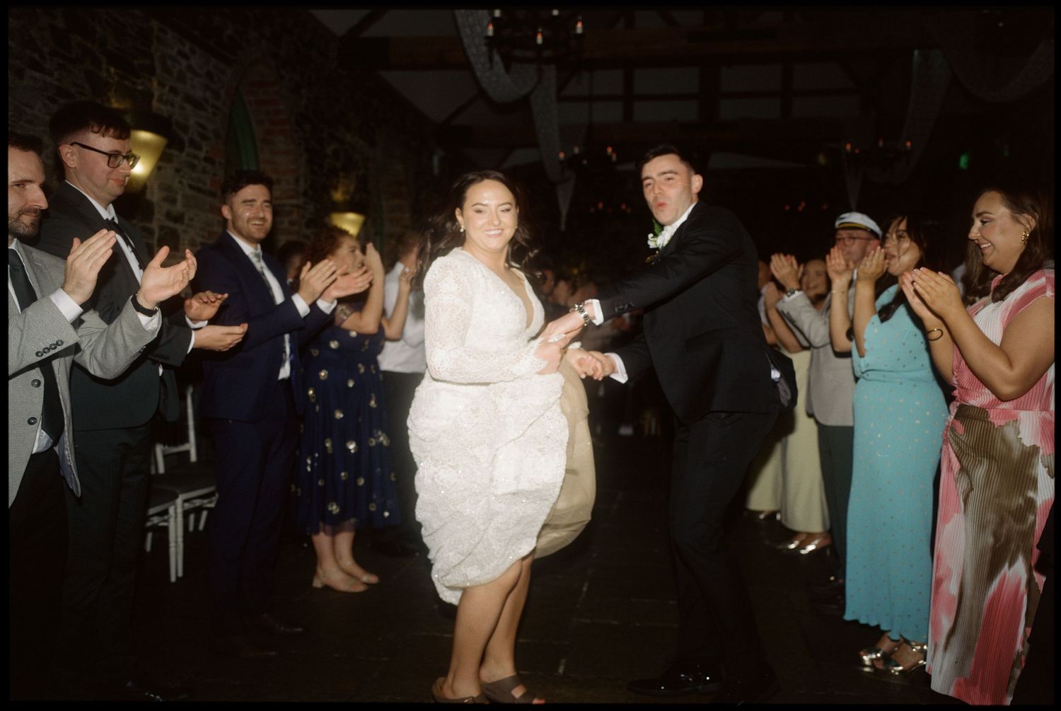 Wedding reception dance floor filled with guests celebrating under dim lighting.