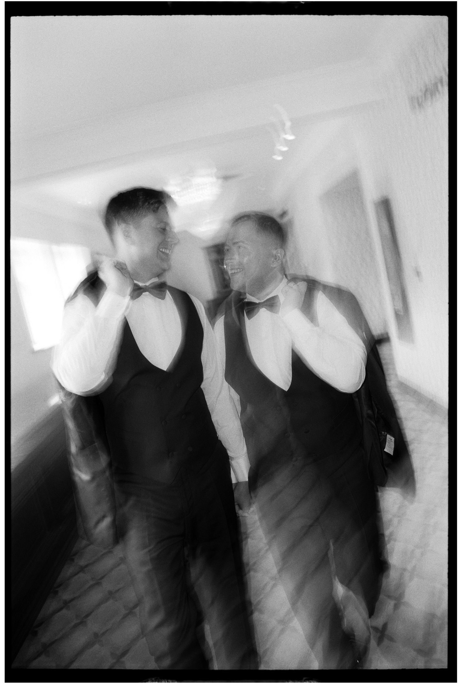 Blurred black and white motion photograph showing figures in formal wear moving through a bright interior space.