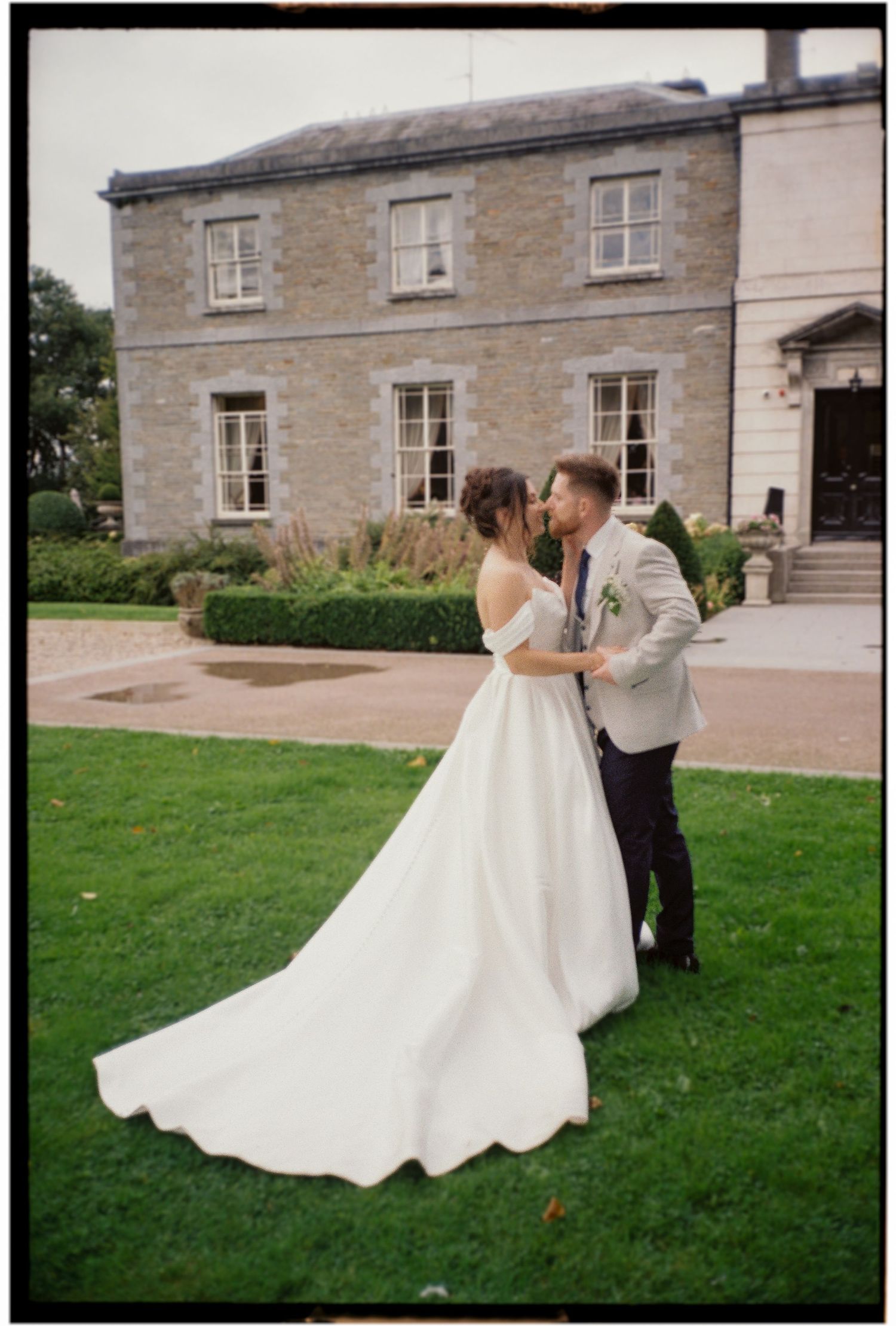 A romantic moment between newlyweds on the lawn of a historic stone building.