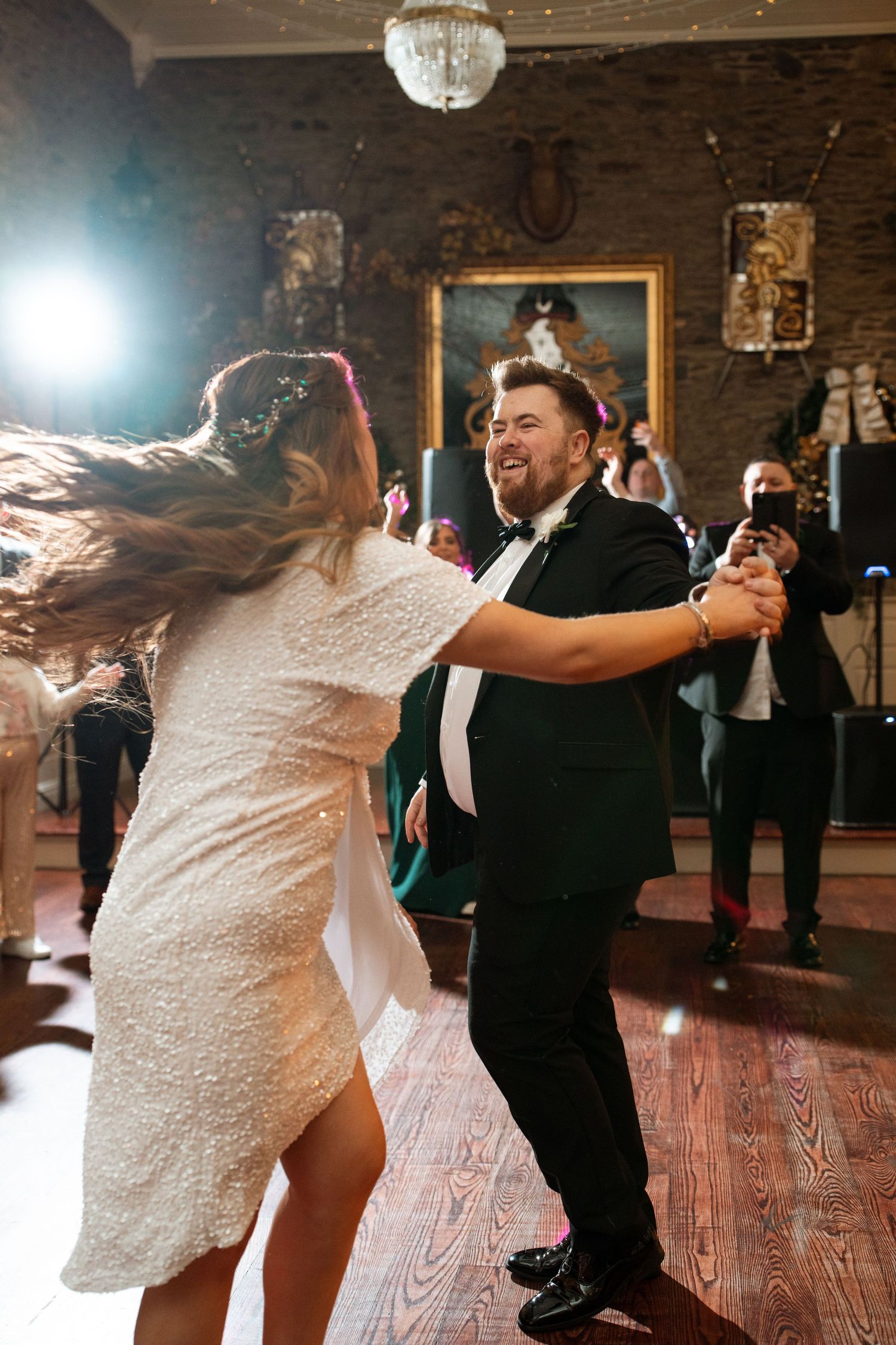 Energetic wedding dance floor moments captured in a rustic venue with wooden floors.