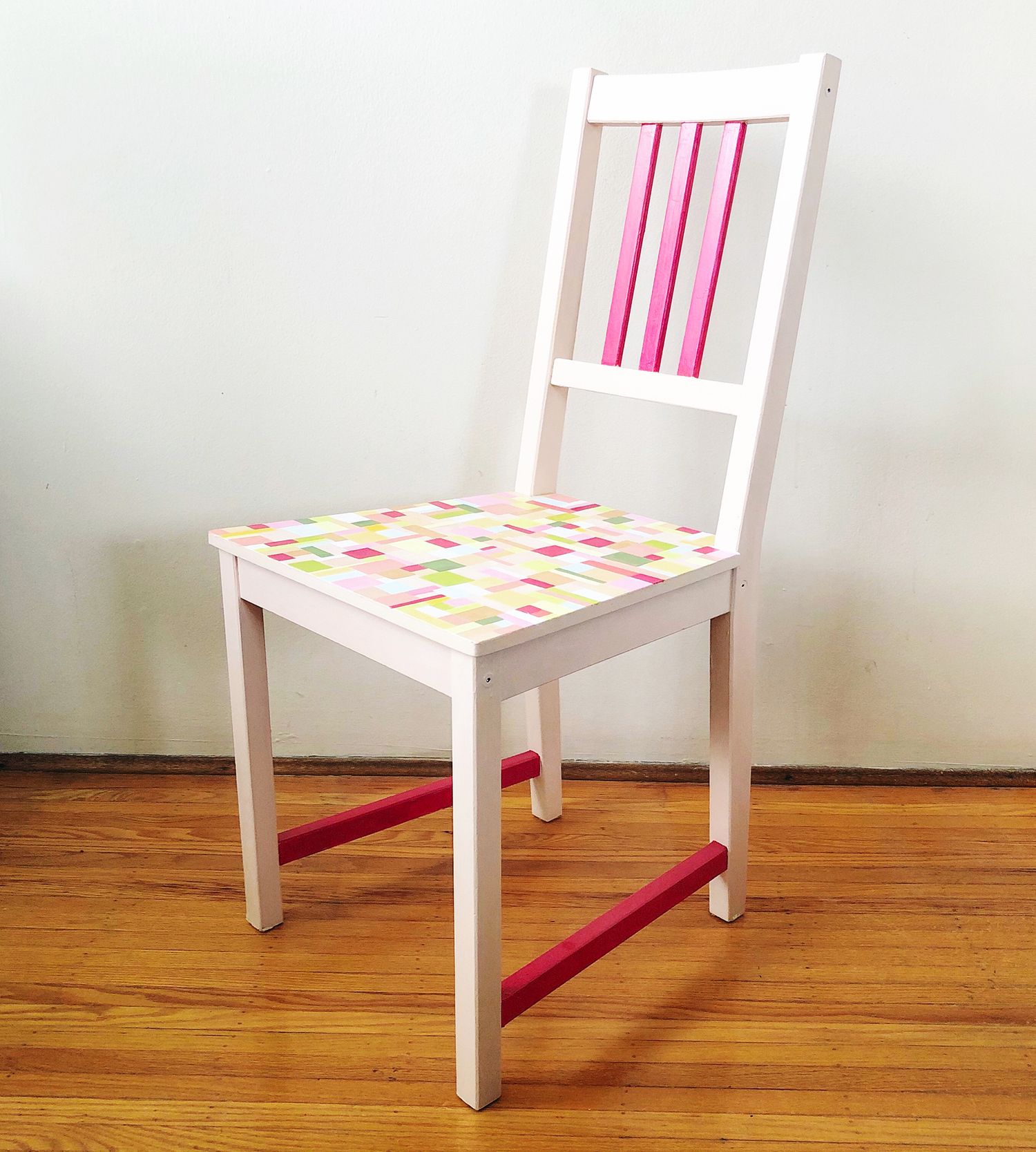 White painted wooden chair with colorful geometric patterned seat cushion and pink accent rails on hardwood floor.