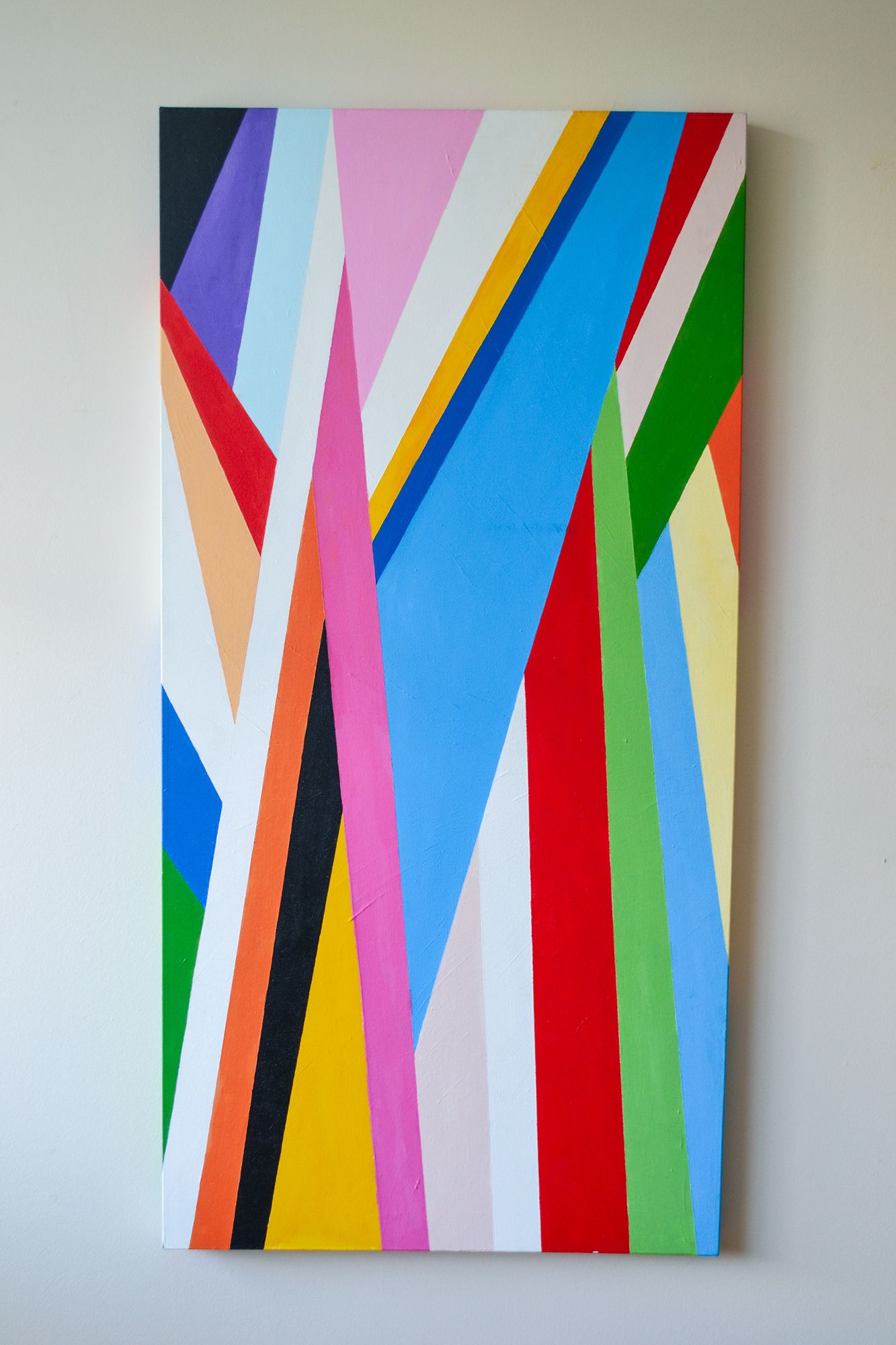 Colorful abstract painting with diagonal geometric stripes in rainbow colors displayed on a white wall.