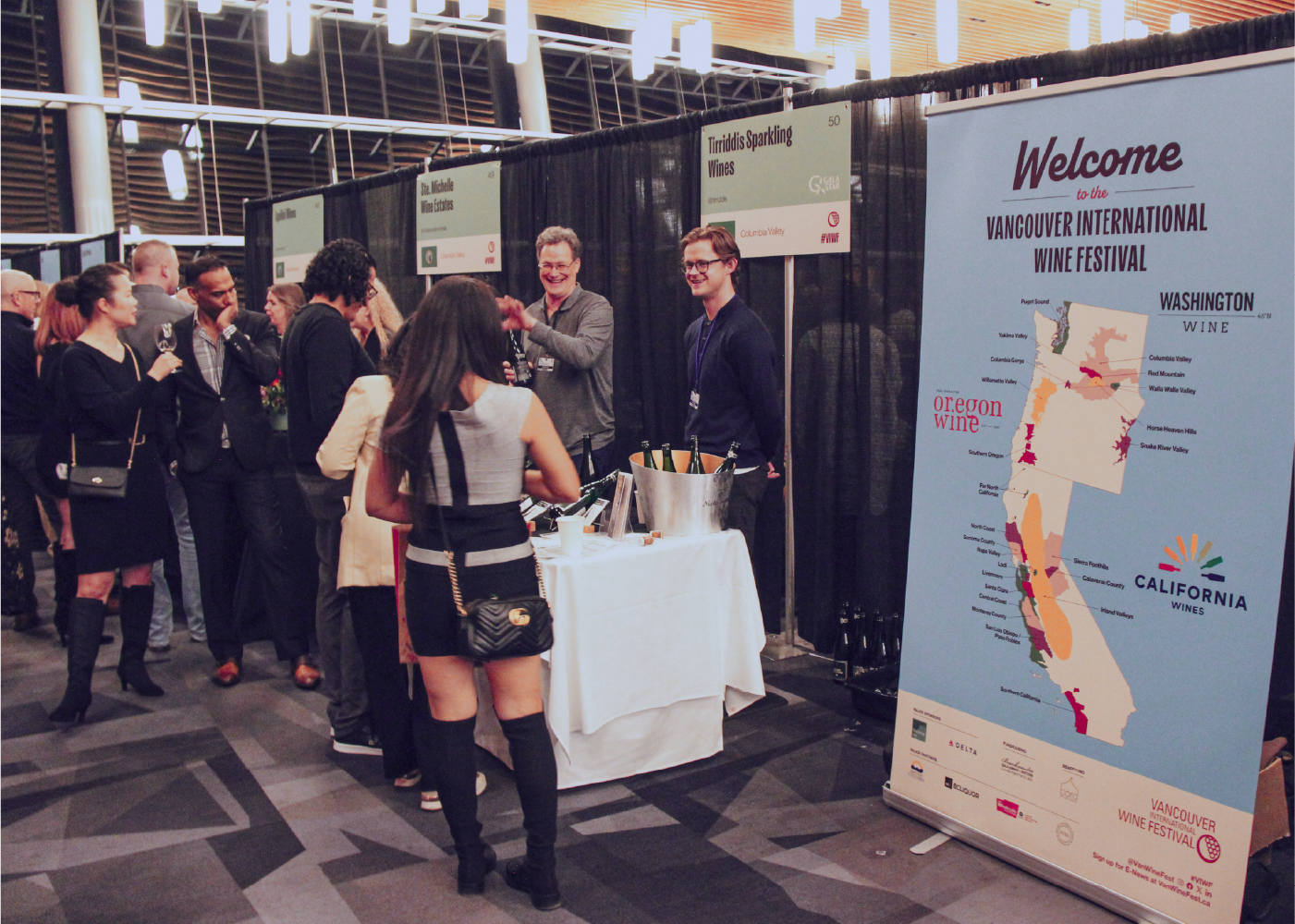 Guests mingling in the tasting room at the Vancouver International Wine Festival with regional wine maps displayed.