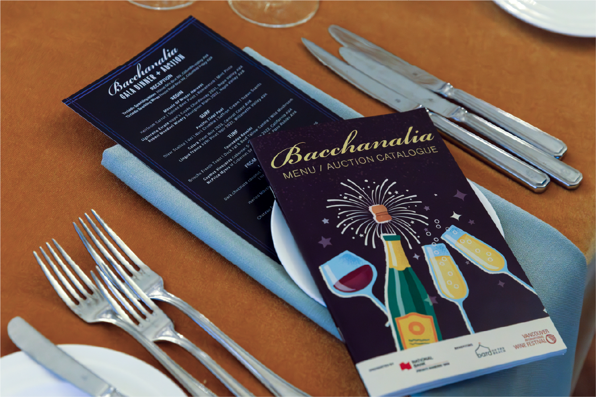 Illustrated Bacchanalia Gala menu and auction catalogue on a table with silverware and champagne glasses.