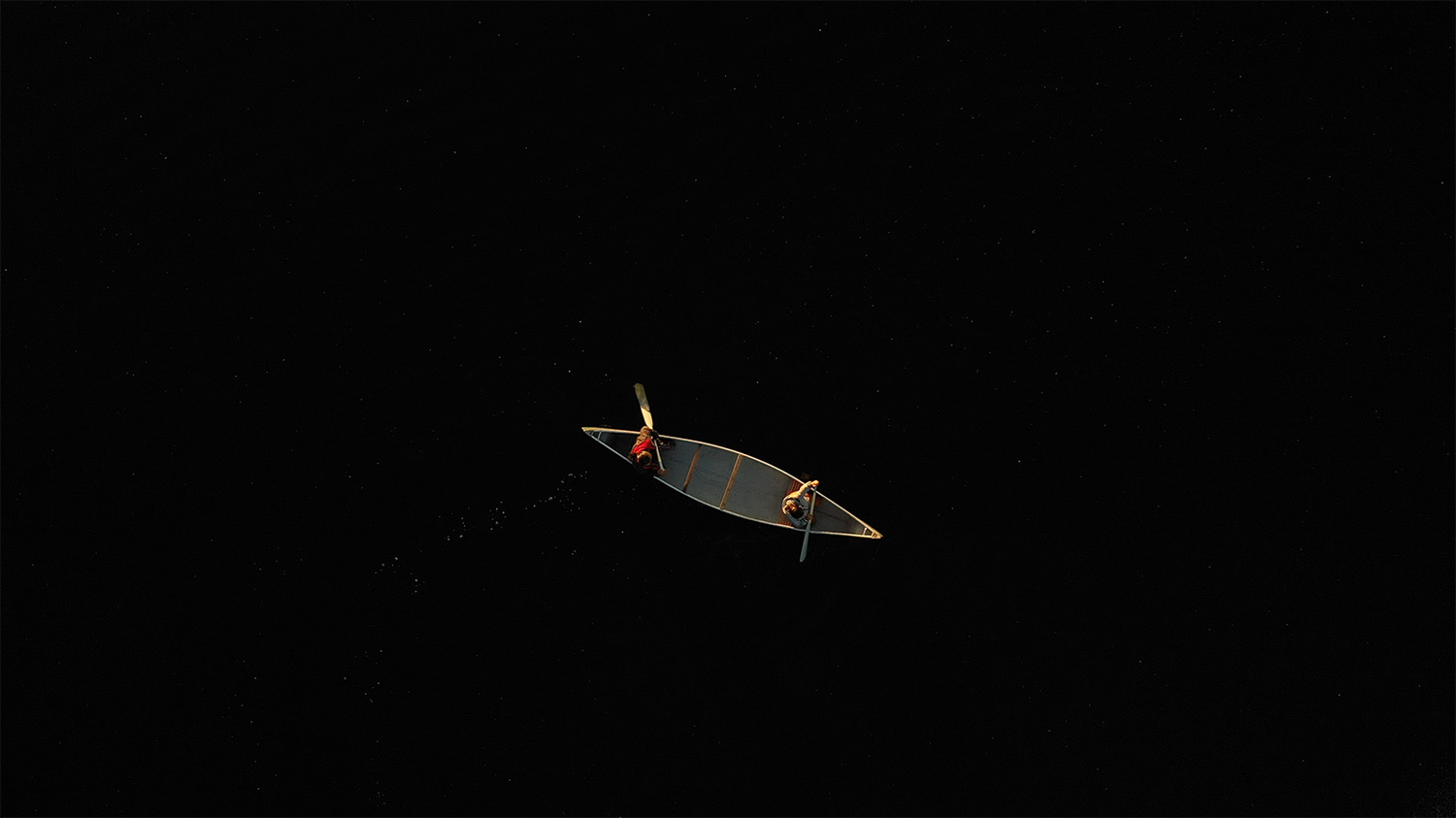 Aerial view of a lone wooden boat with two rowers.
