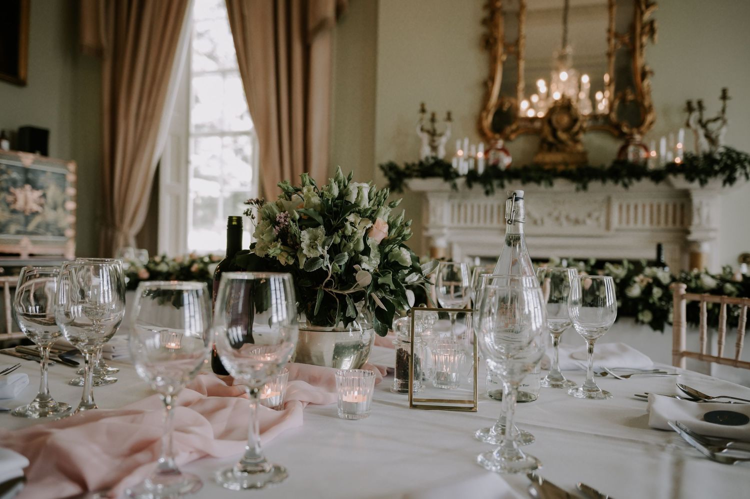 Elegant wedding reception venue with crystal chandeliers, pink drapes, and tables set with floral centerpieces.