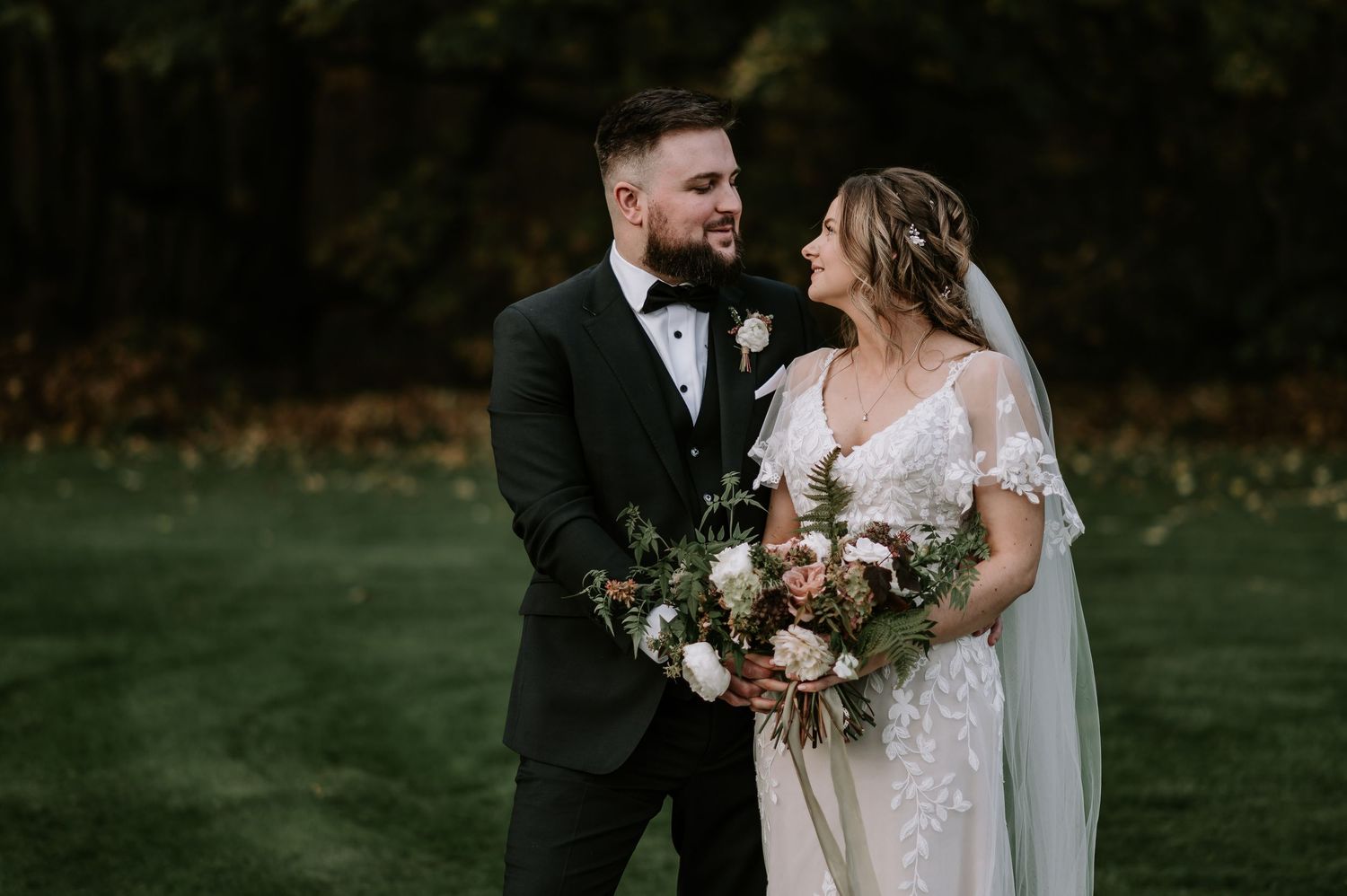 Bride and groom embrace during intimate outdoor forest wedding ceremony with autumn foliage in background.