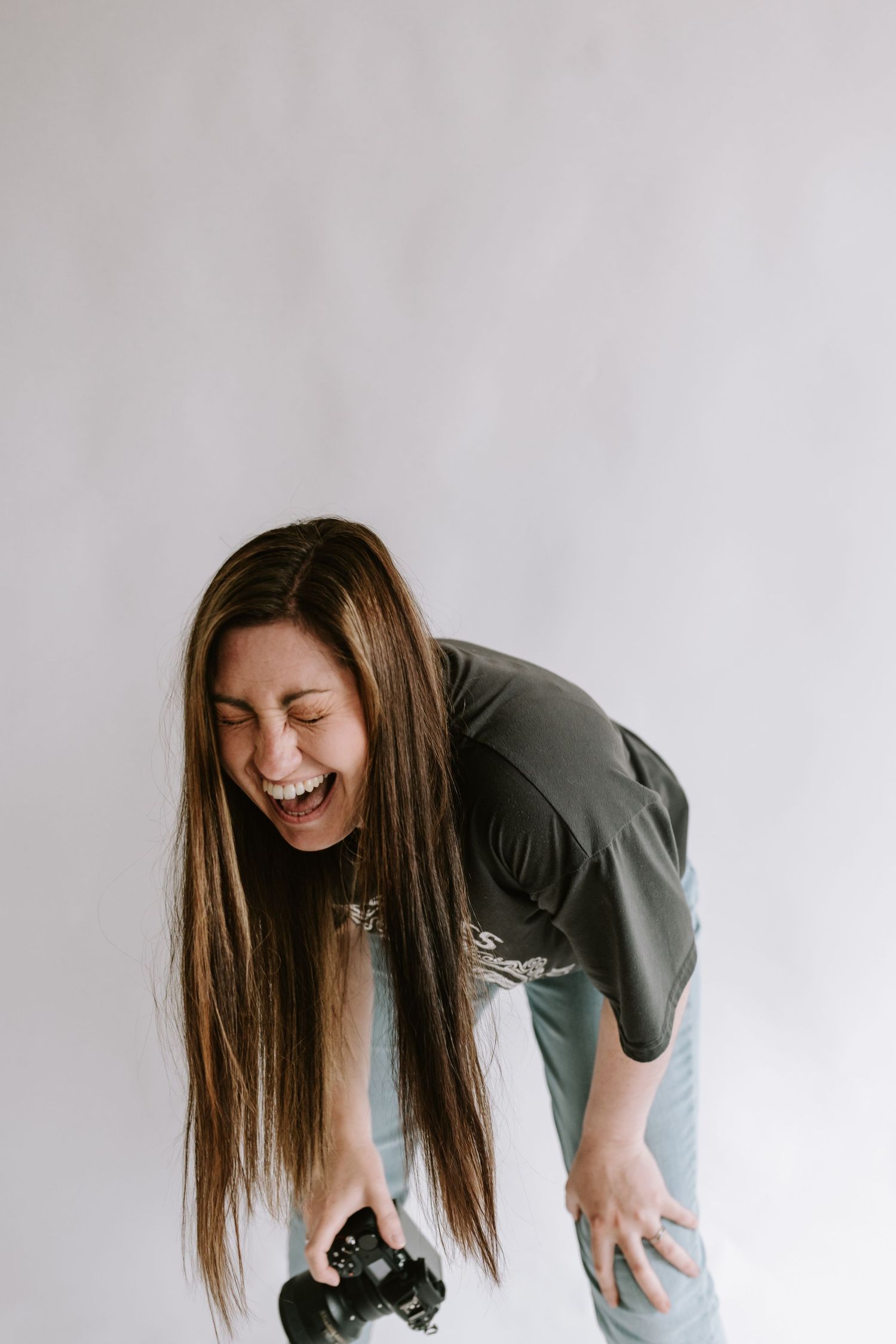 Photographer in olive green shirt bends over laughing while holding camera against white background. Melton Mowbray photoshoot