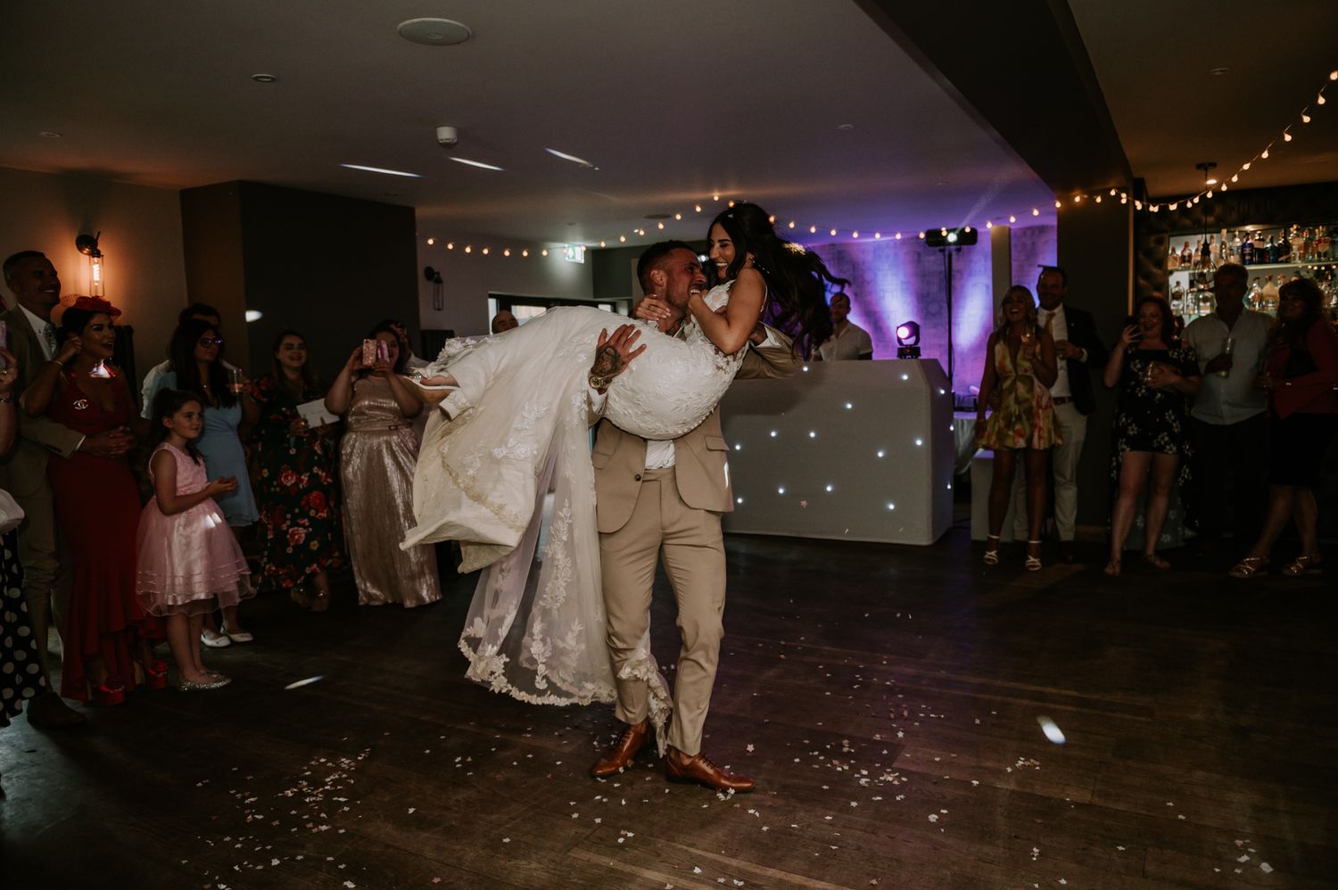 A wedding couple shares their first dance on a dimly lit reception floor decorated with twinkle lights and romantic ambiance.