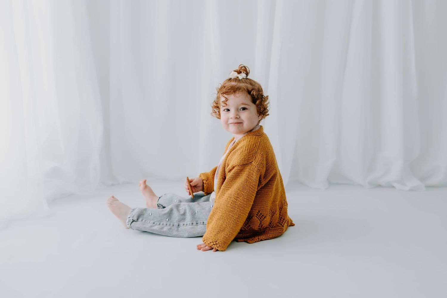 Toddler in mustard yellow sweater sitting on white backdrop, studio, Melton Mowbray.