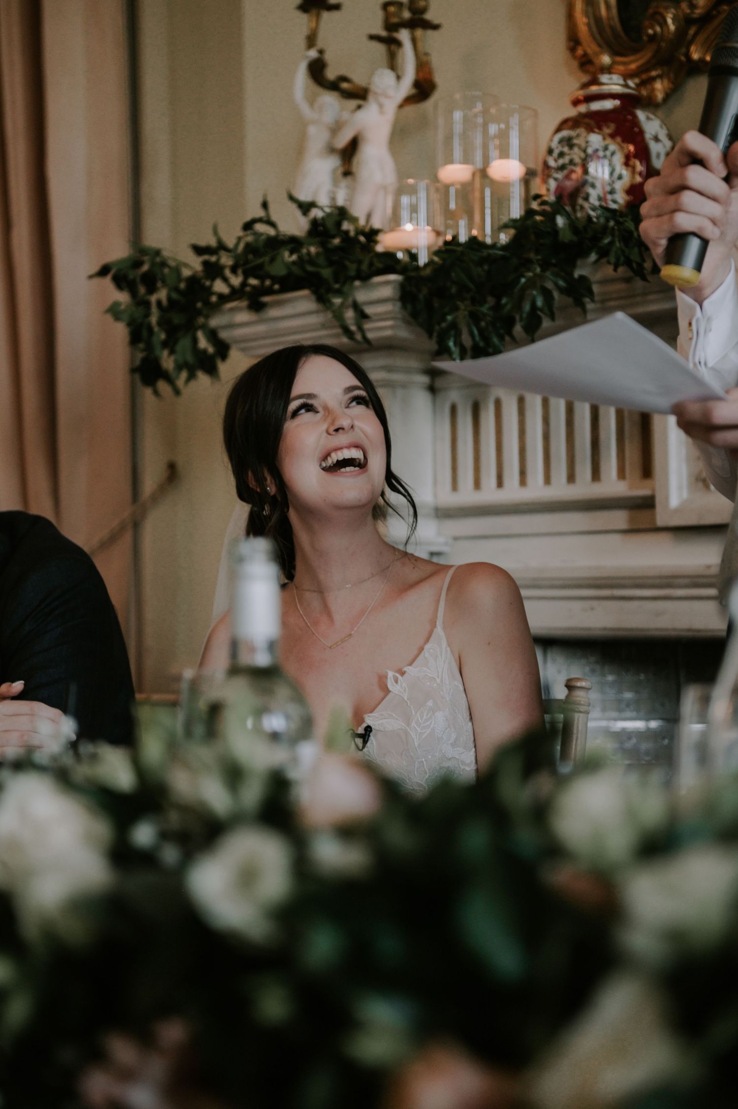 A candid moment of joy and laughter captured during a dimly lit reception with candles and greenery decorations.