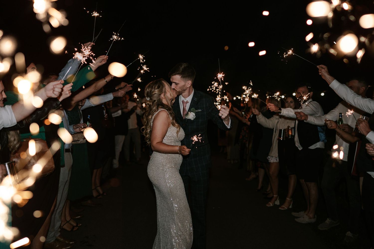 Wedding guests wave sparklers in the dark during an outdoor nighttime celebration send-off.