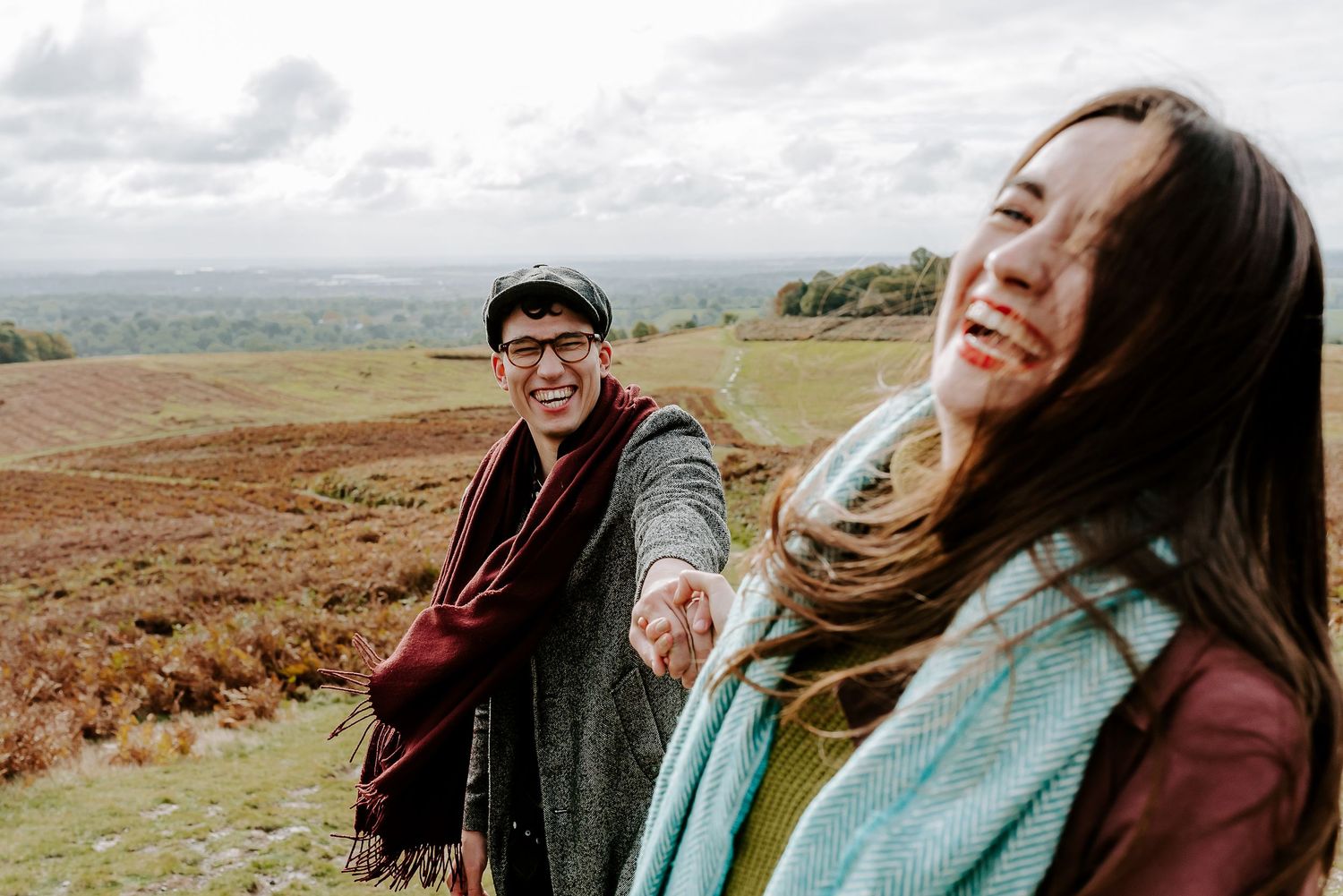 Two people share a joyful moment together while hiking on a scenic hilltop overlooking a vast countryside landscape.