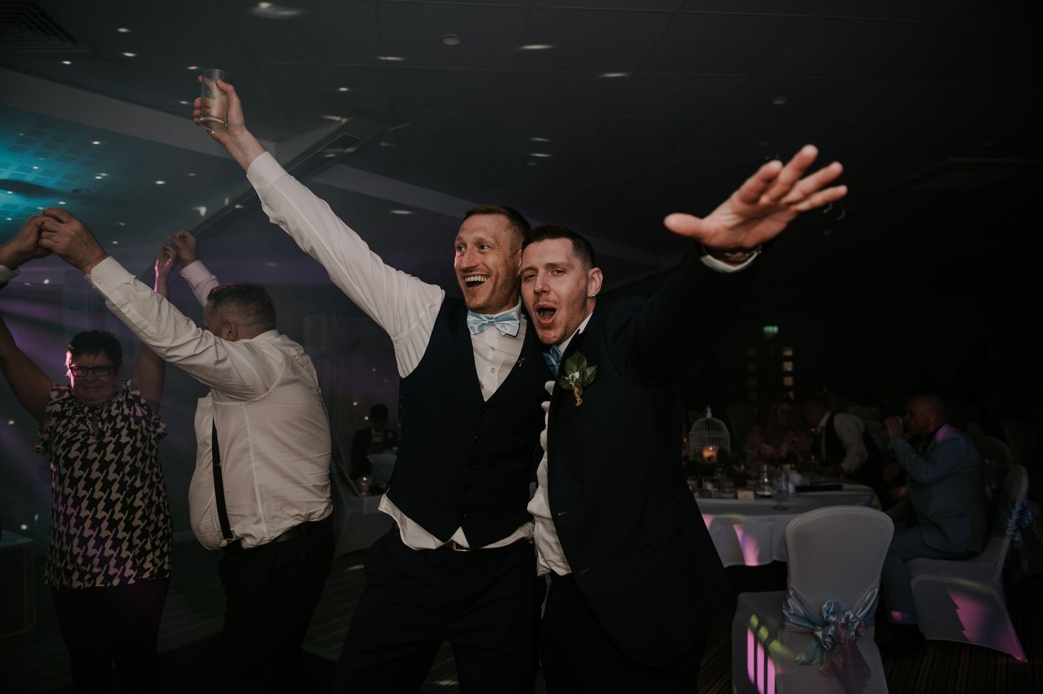 Wedding guests dancing and celebrating on a dimly lit dance floor at a reception party.