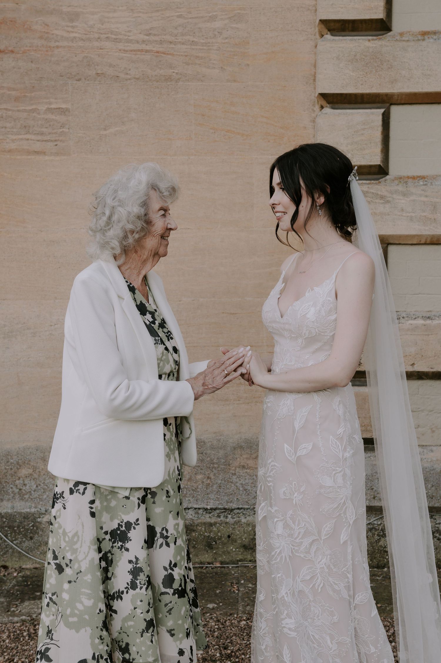 A touching moment between two women in formal attire exchanging stories and smiles against a textured wall.