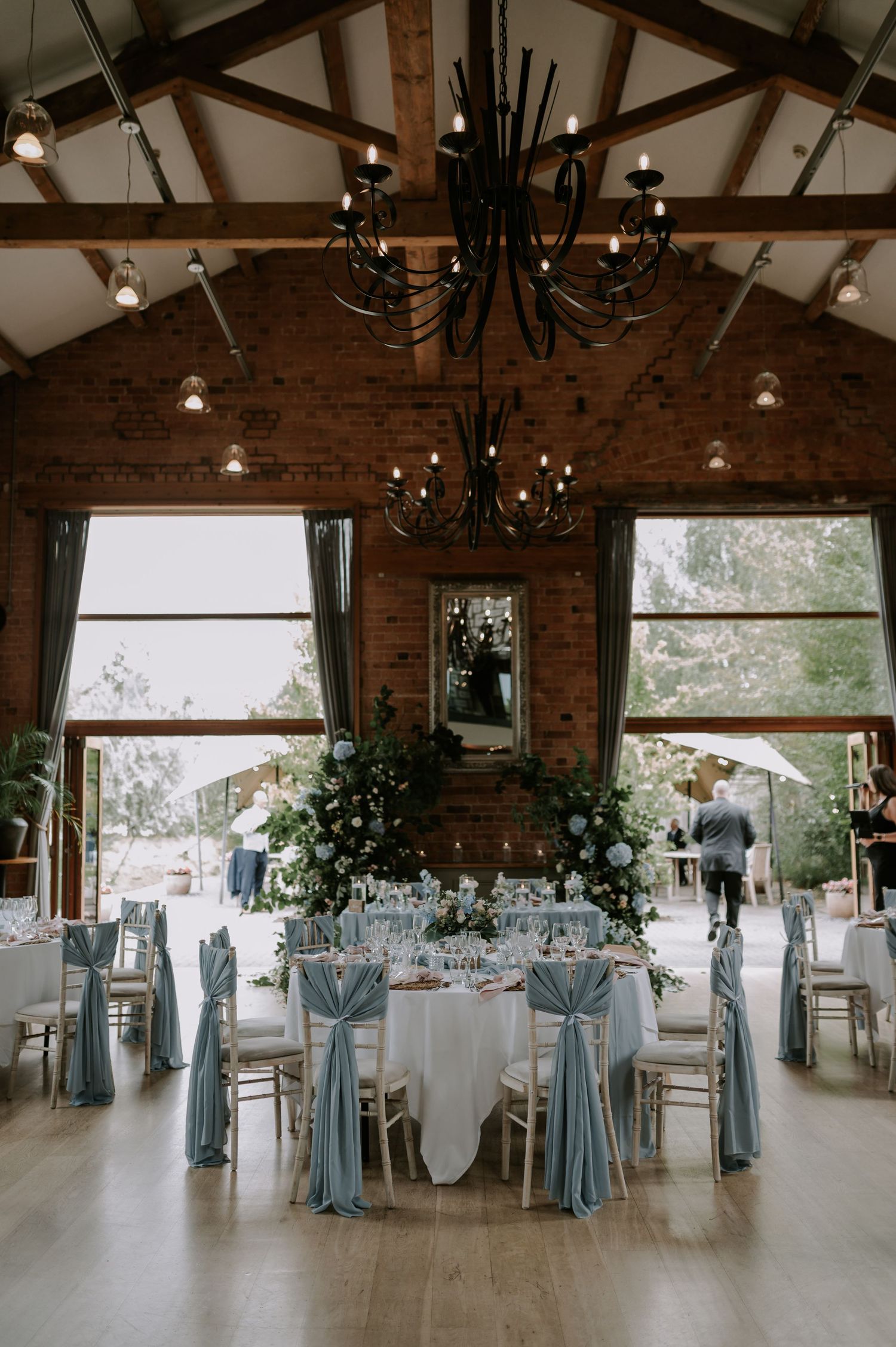 Panoramic view of an elegant wedding reception venue with exposed brick walls, chandeliers, and blue-accented table settings.