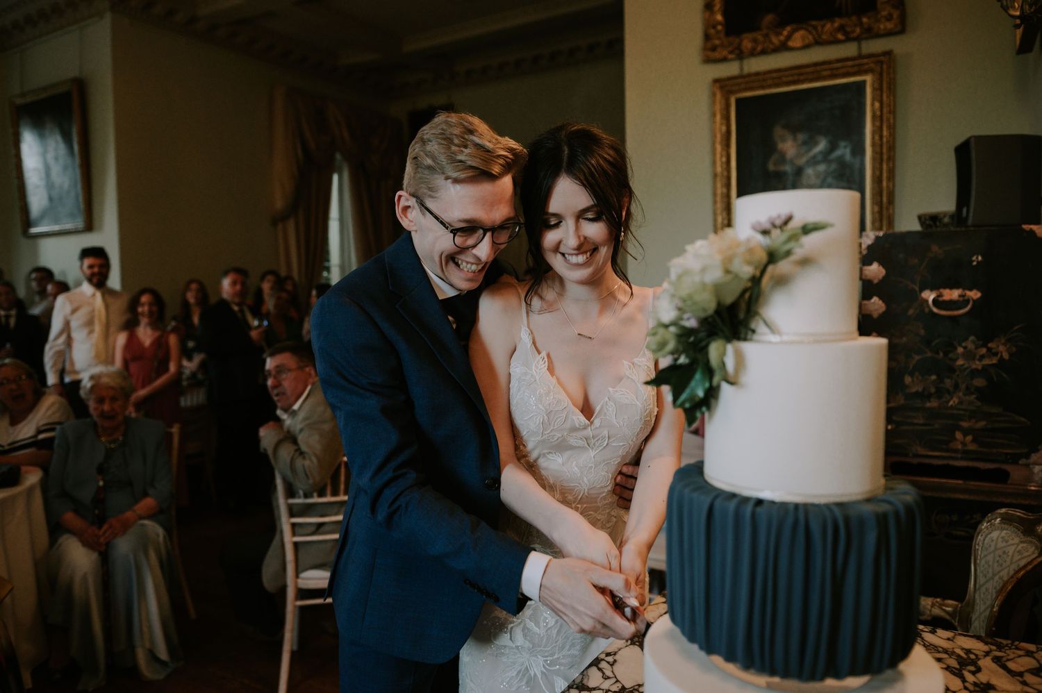 A couple shares a tender moment while cutting their white wedding cake at their elegant reception celebration.