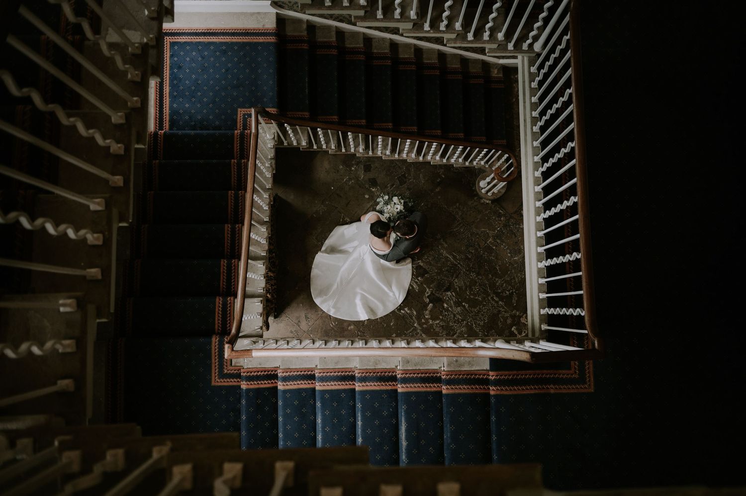 Looking down a spiral staircase in a building with dark metal railings and geometric patterns creating depth.
