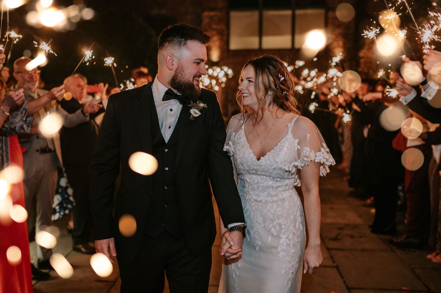 A couple walks through a tunnel of sparklers at their wedding ceremony while sharing an intimate moment together.