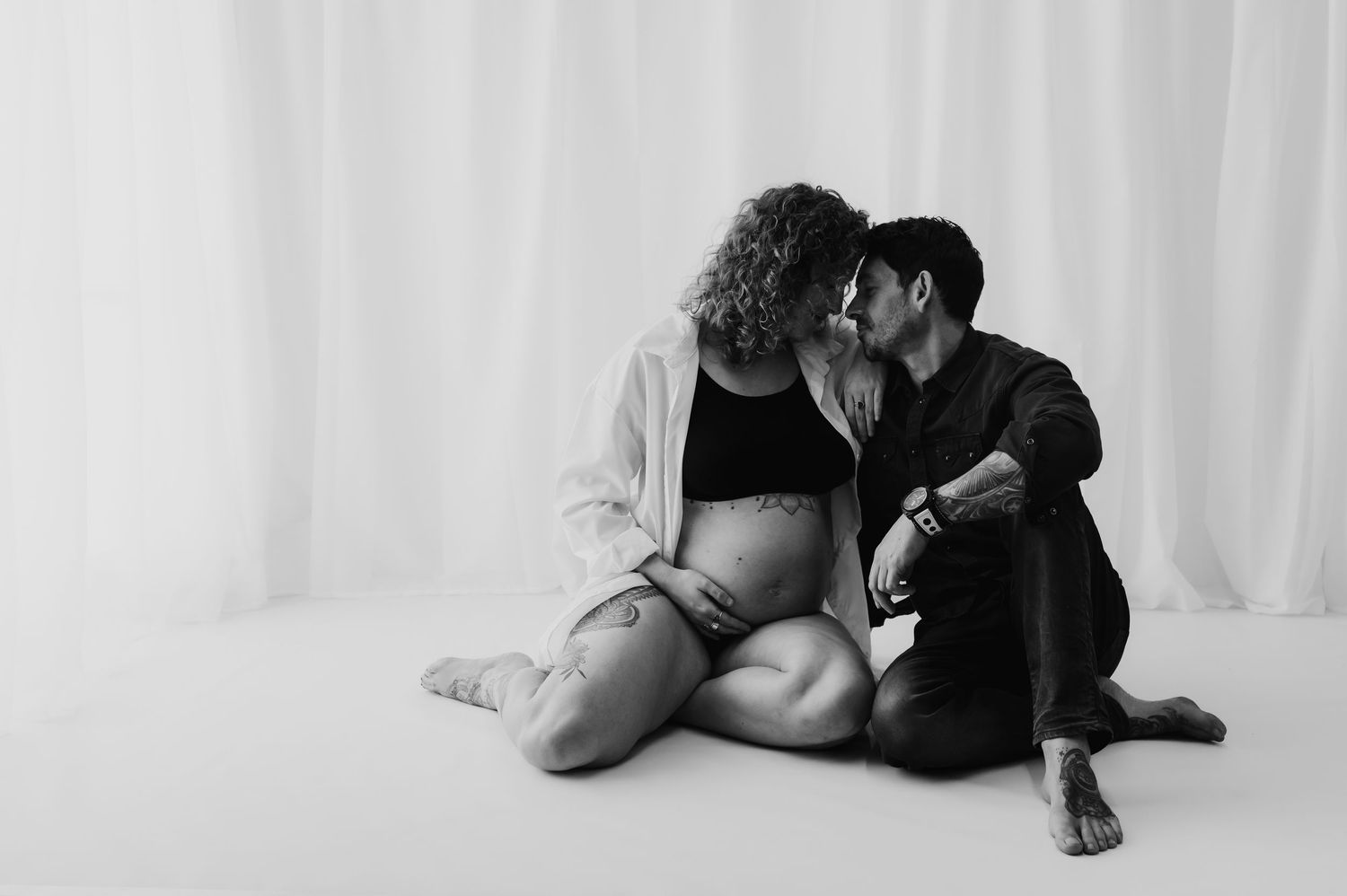Couple sat on floor in close embrace, black and white maternity image, studio, Melton Mowbray.