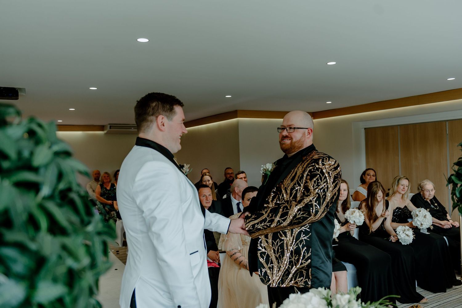 Two people interact during a special ceremony while guests look on in the background at an indoor venue.