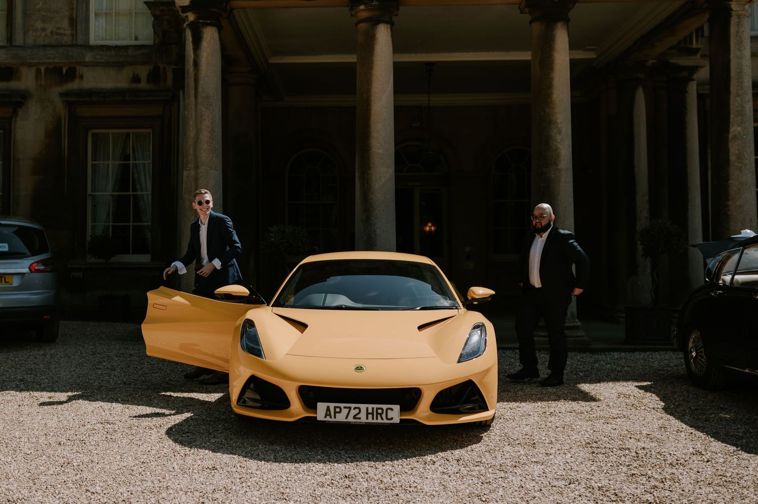 An elegant yellow sports car parked in front of a historic stone building with classical architecture details.