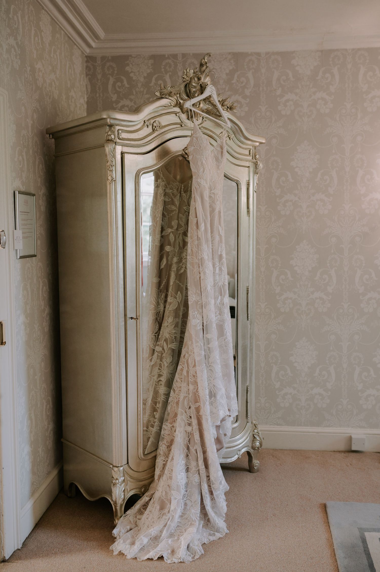 Elegant white vintage wardrobe sits against floral wallpaper in an empty Victorian-style room interior.