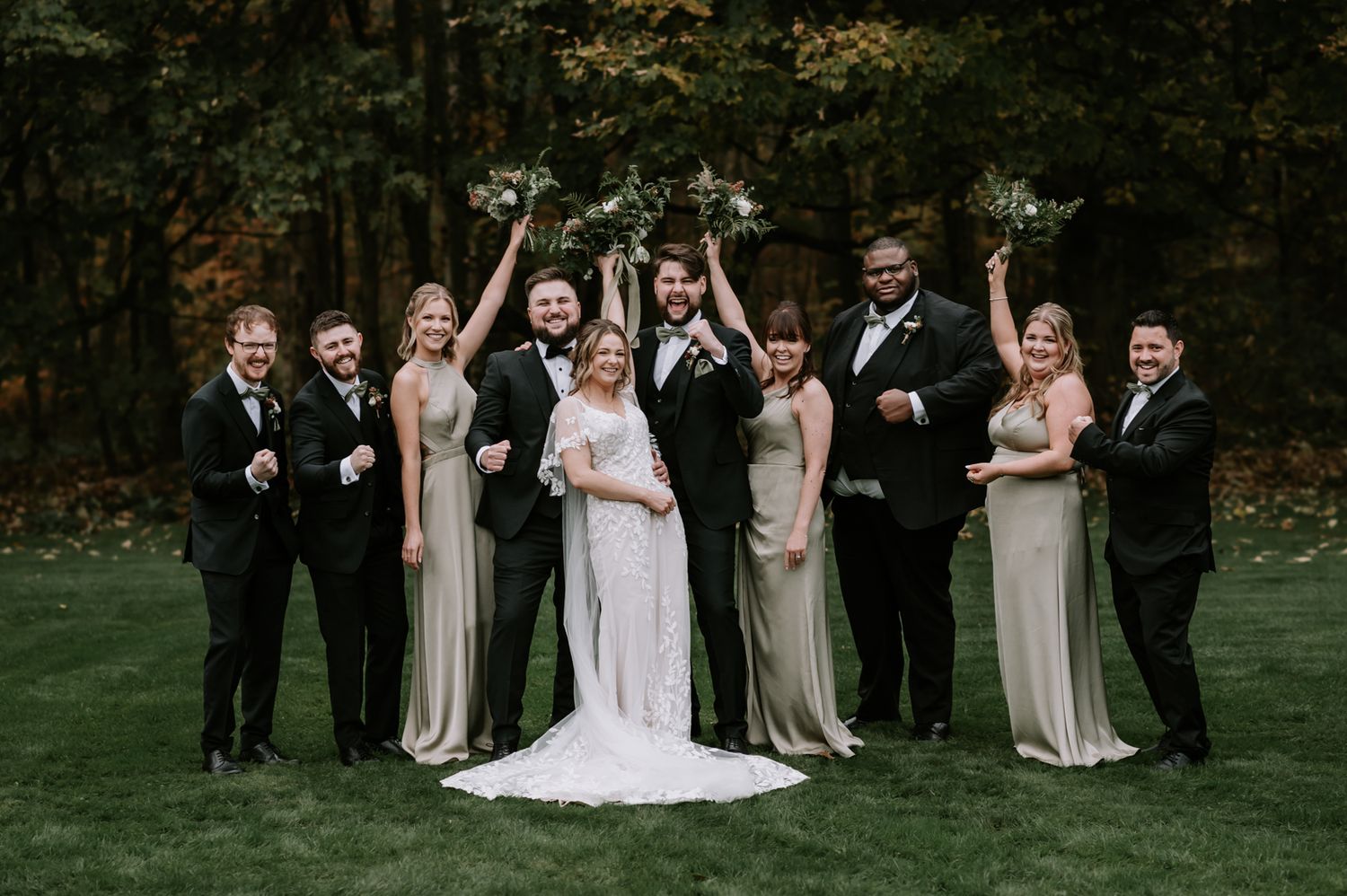 A group photo of wedding party members in formal attire standing together outdoors in a garden setting.