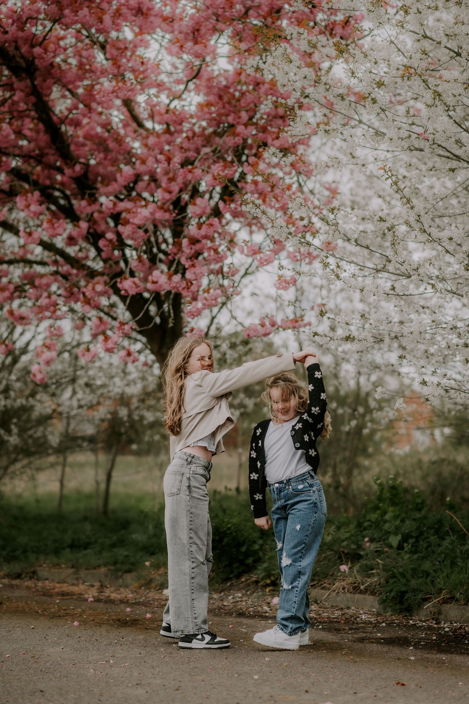 Two girls dancing together under blooming pink and white cherry blossom trees in spring.