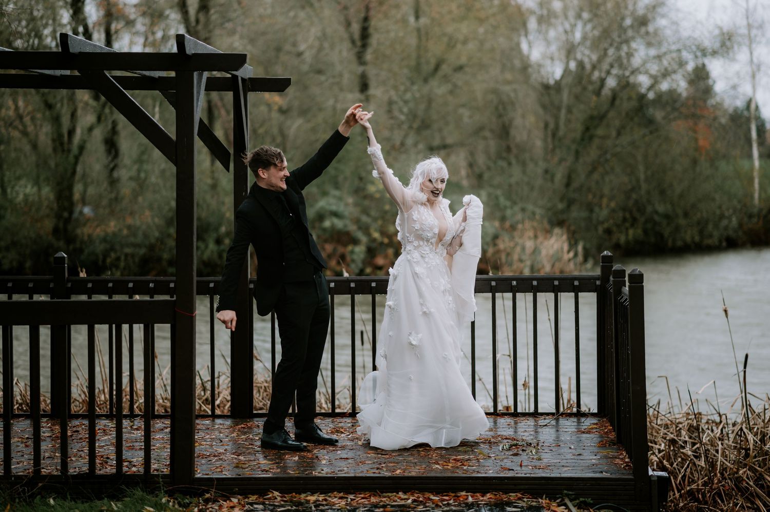 Two people dance together on a wooden deck by a lake during an overcast winter day.