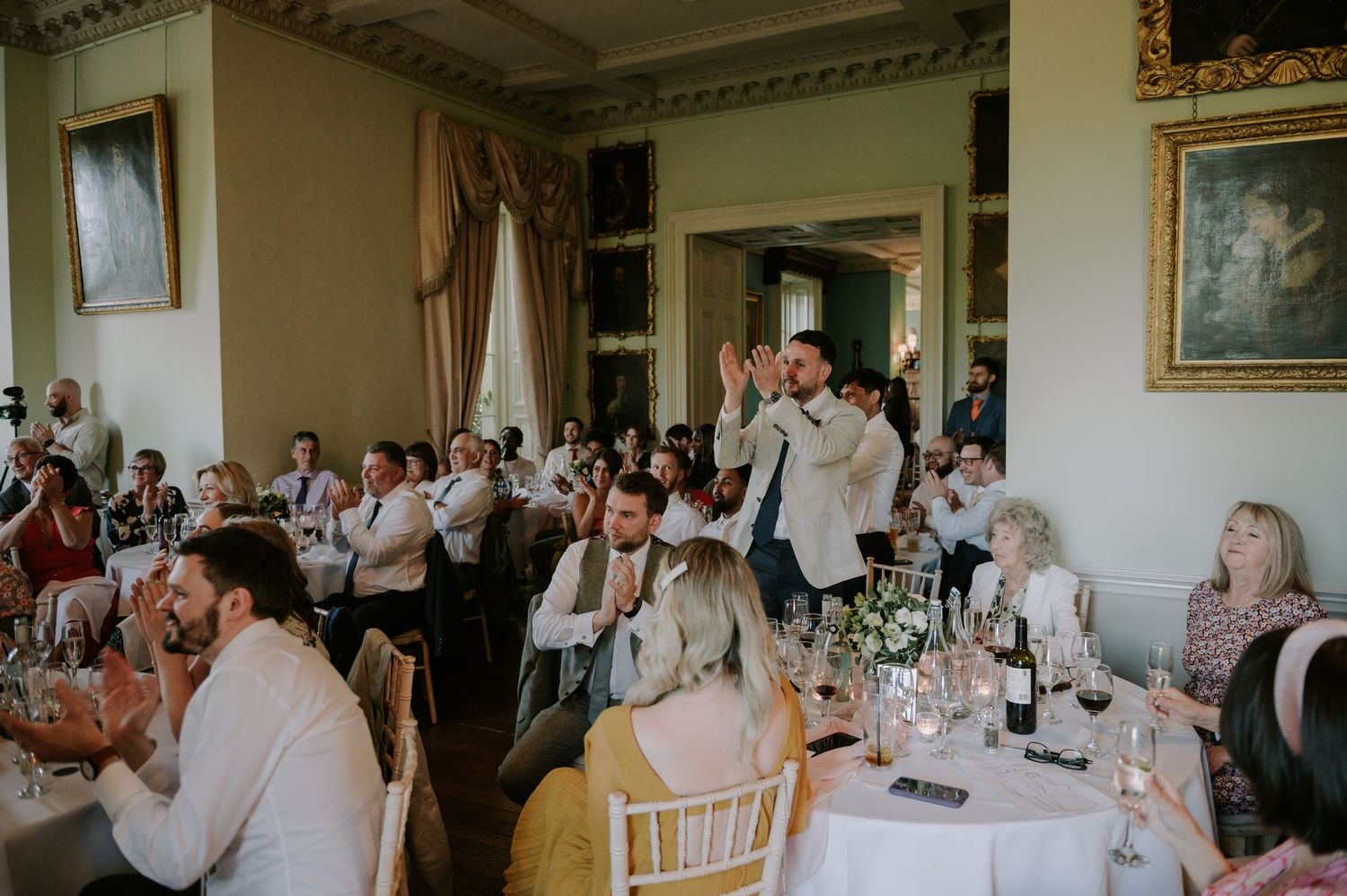 Wedding guests sit at decorated banquet tables inside an elegant reception hall during a formal celebration.