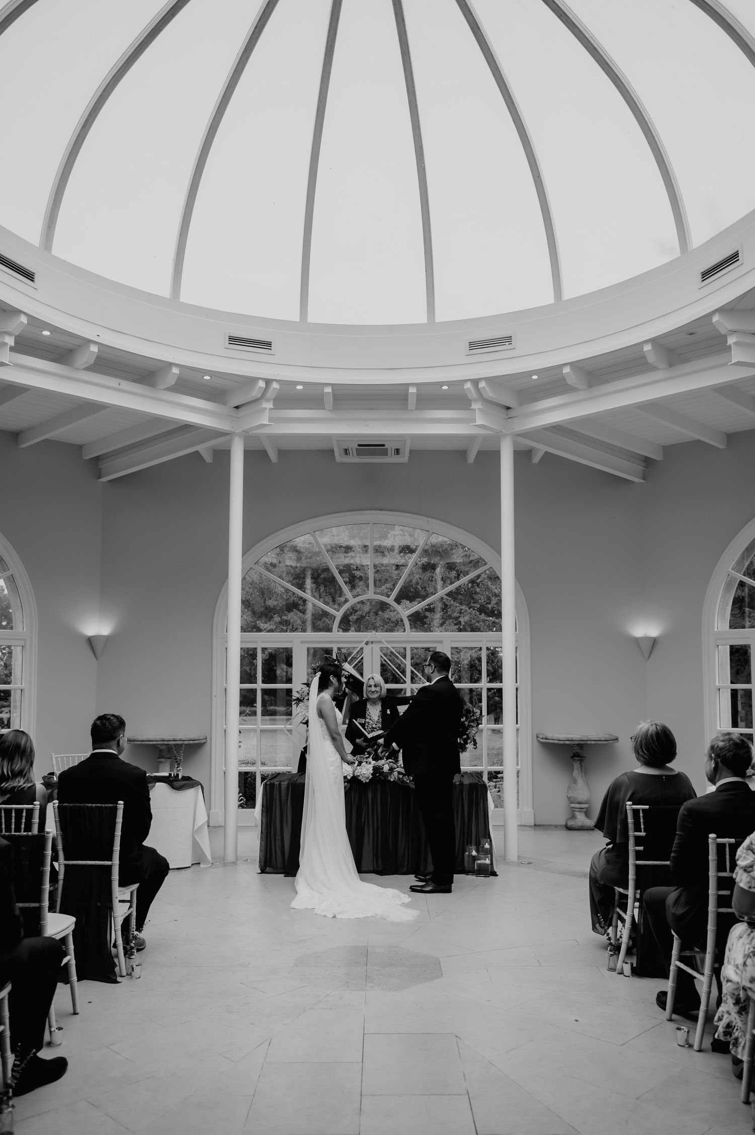 A black and white indoor wedding ceremony in an elegant domed rotunda with arched windows and white pillars.