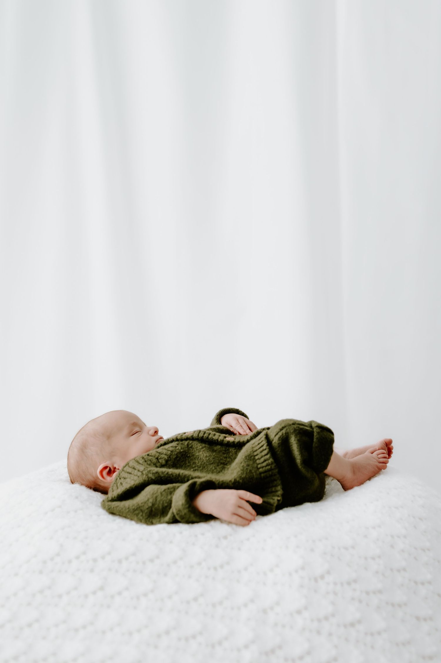 Baby in green knit sweater lying on white surface. studio newborn session, Melton Mowbray.