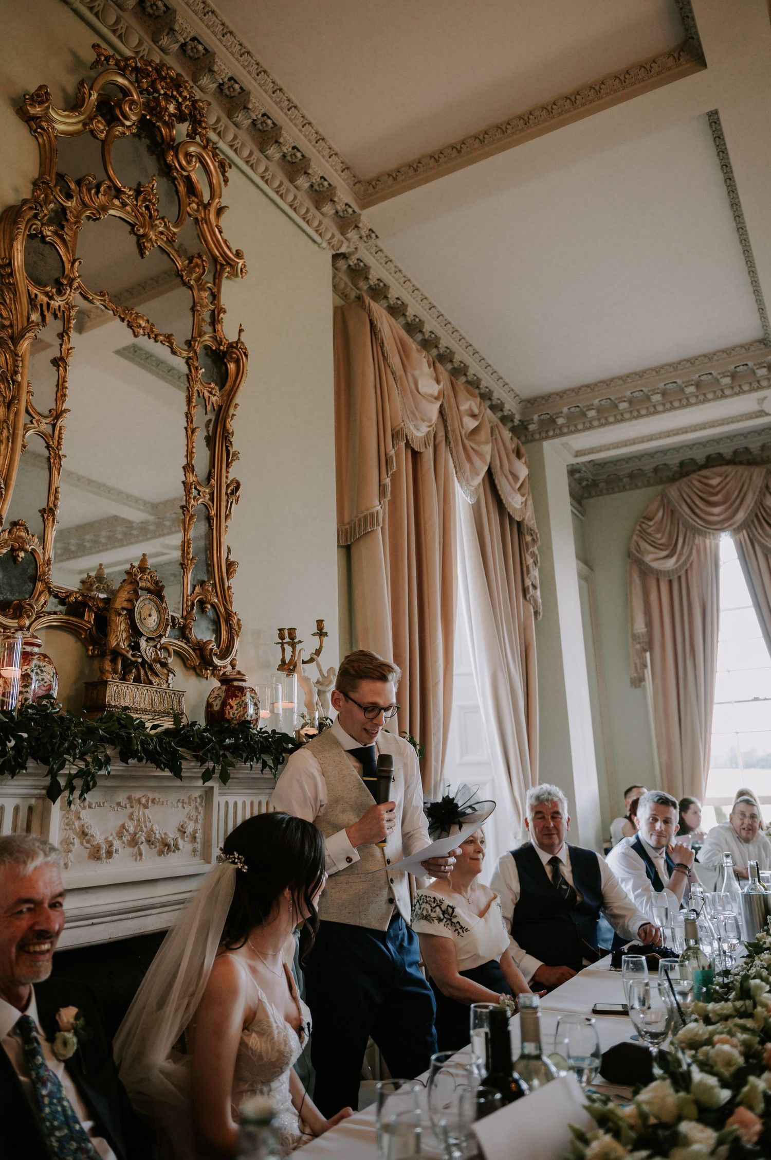 Elegant wedding reception in an ornate room with gold-framed mirrors and white floral centerpieces.